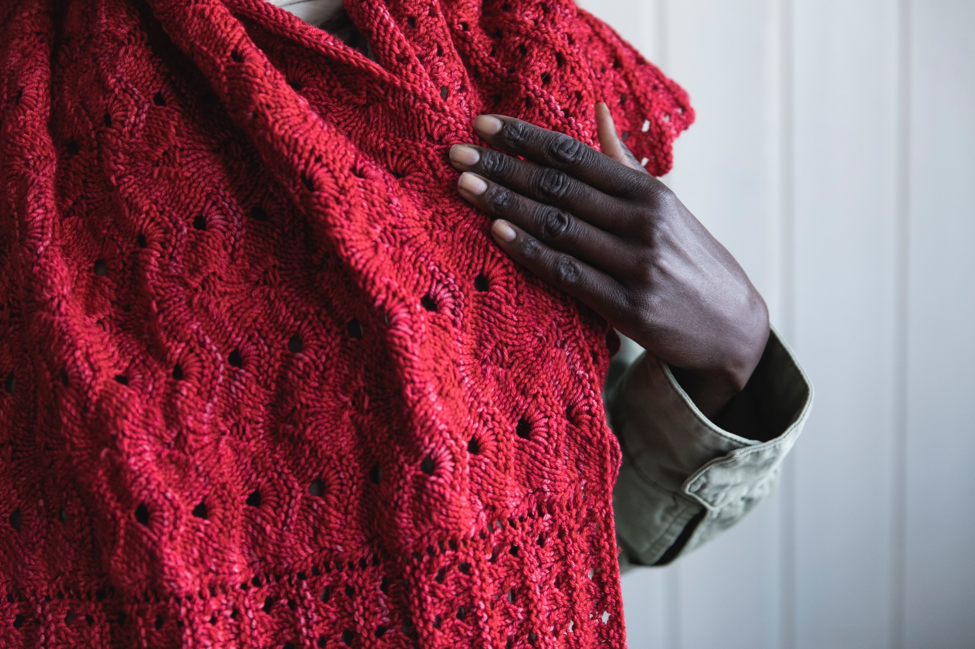 Close up of dark skinned African woman wearing bright red Marjie knitted shawl and khaki coloured jacket 