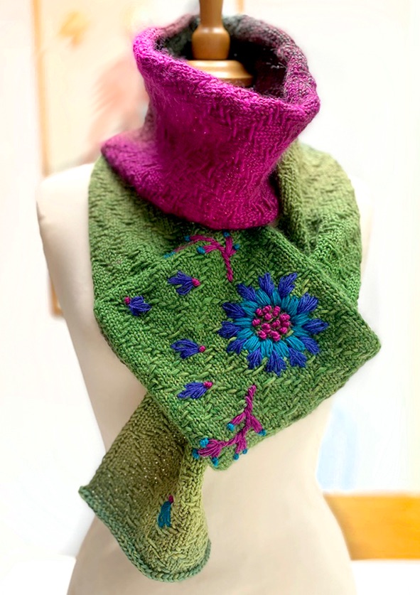 Close up of pink and green gradient coloured knitted and embroidered scarf wrapped around neck of display dummy