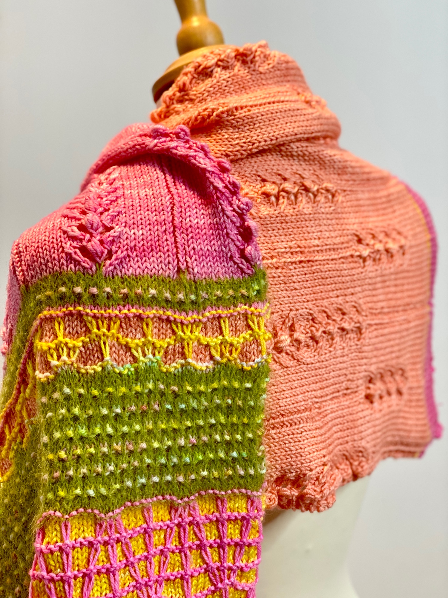 Rear view od a brightly coloured knitted shawl draped over display dummy