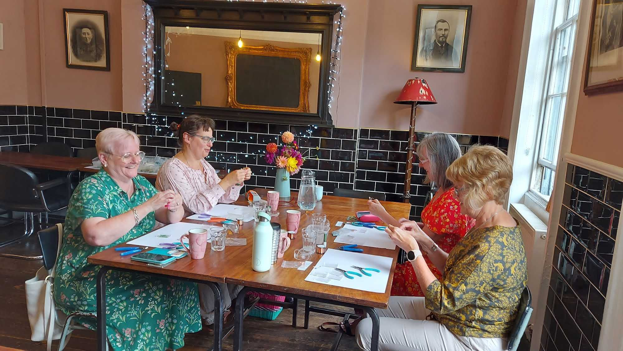 People enjoying a craft workshop sat around a table with tools, beads and wires