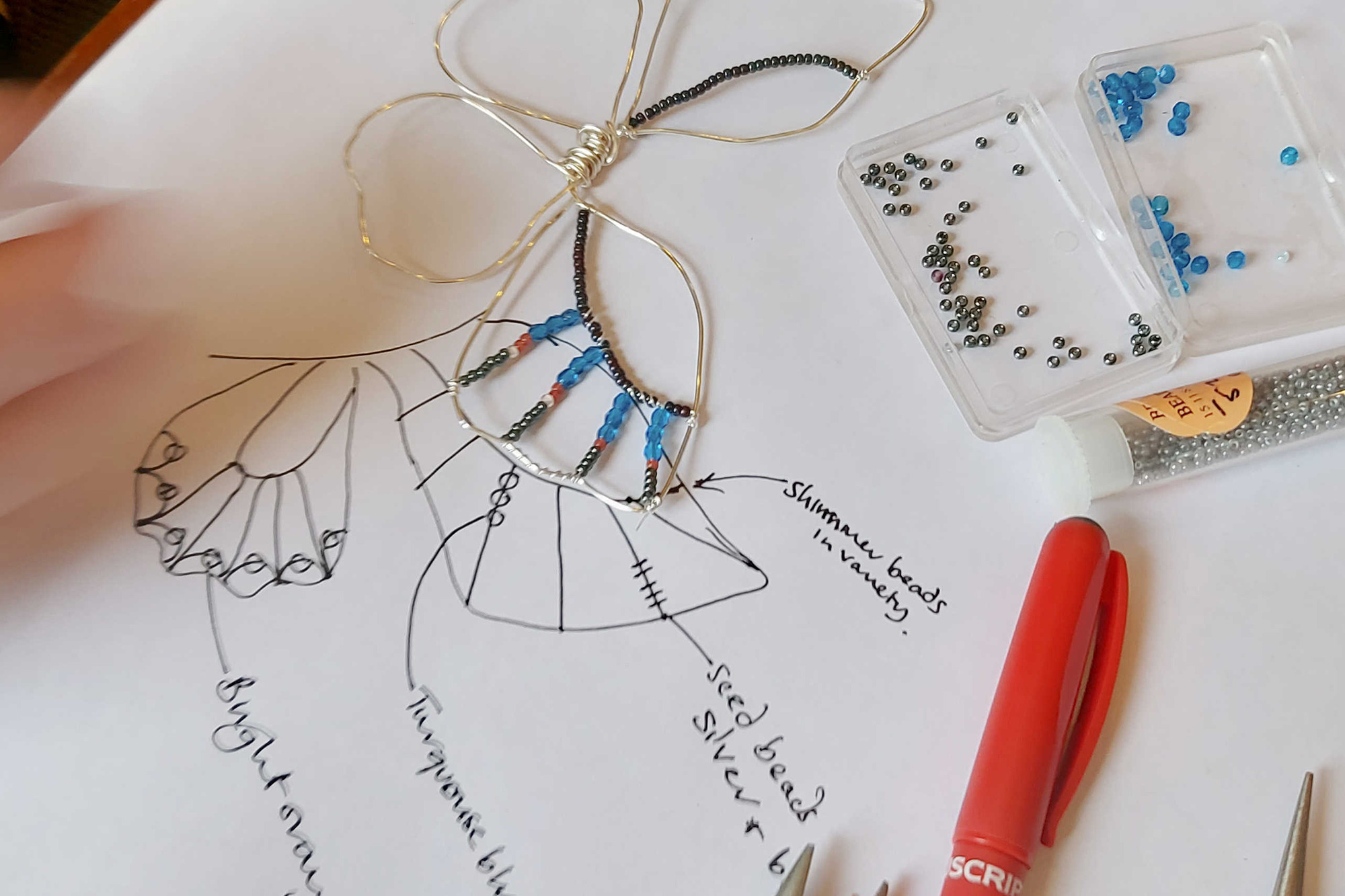 A work table with pliers, a butterfly template and glass beads