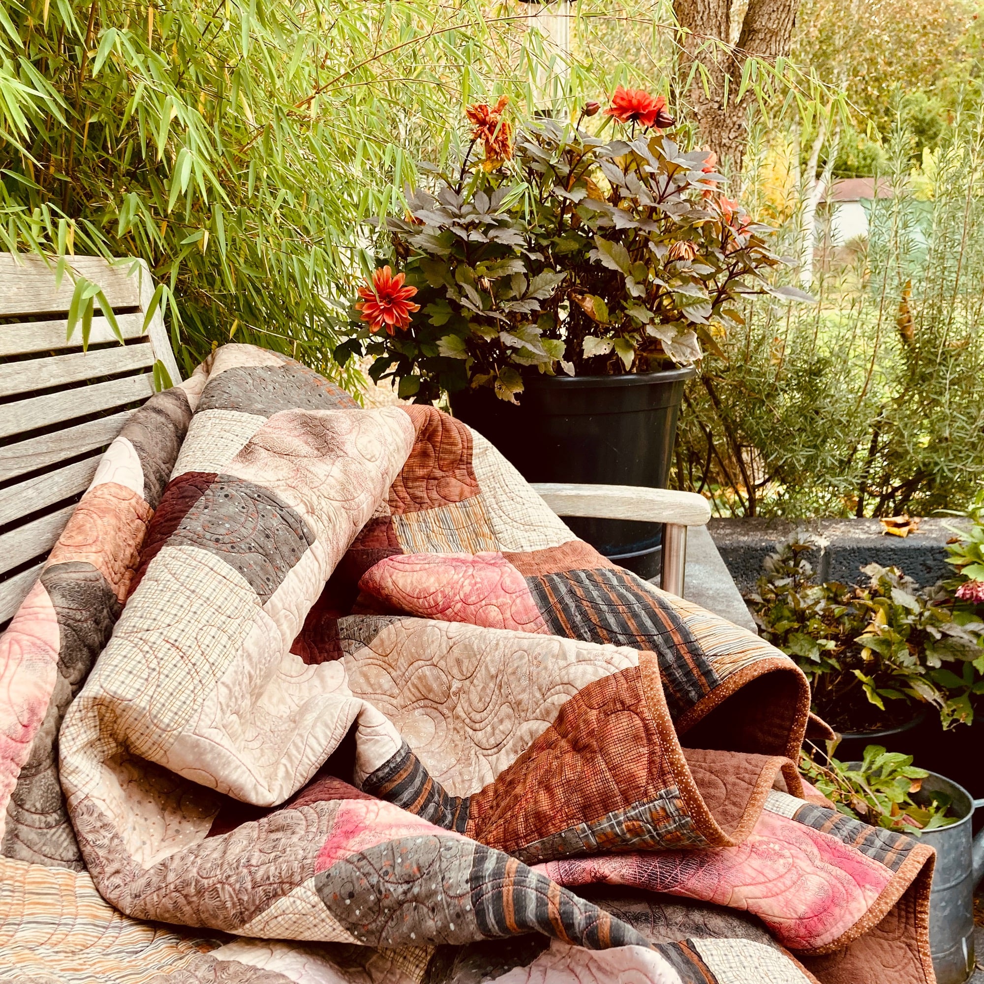 Image of a brown quilt on a bench in a garden 