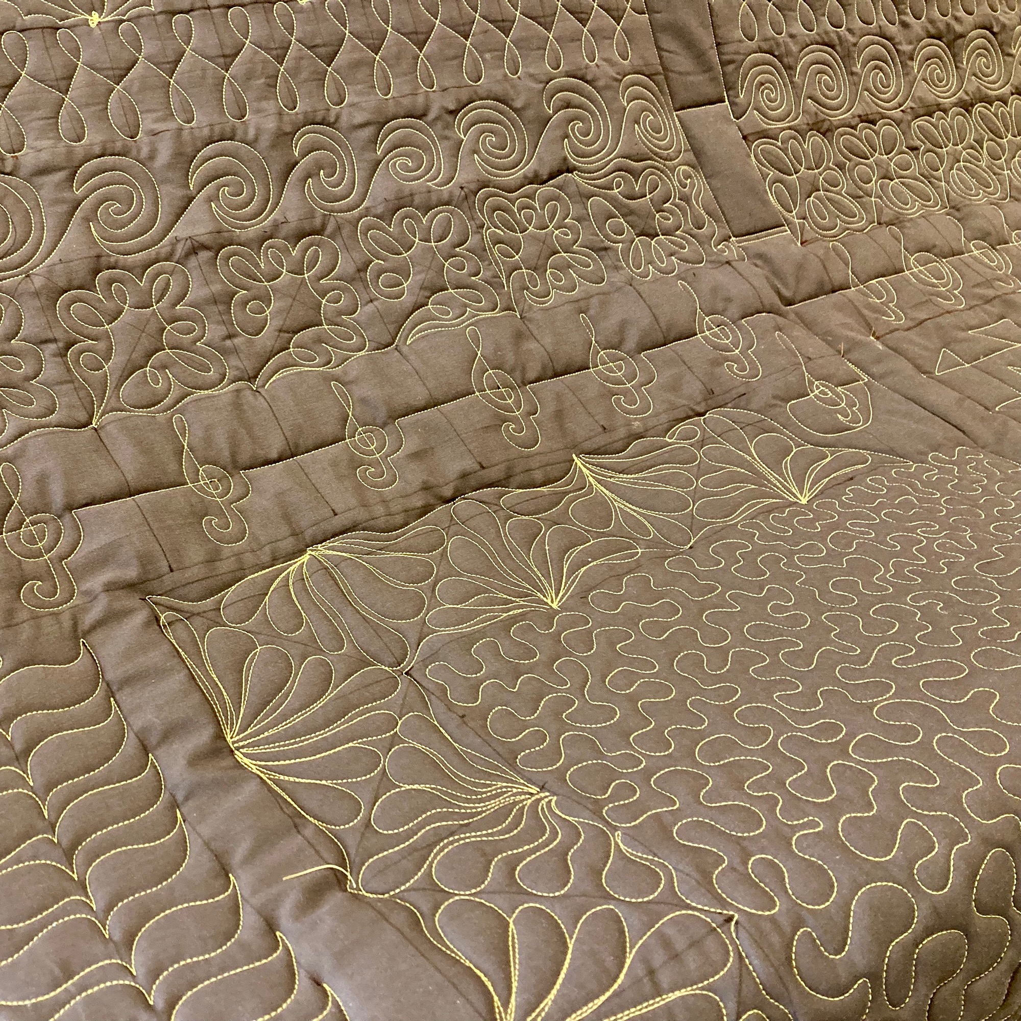 Image of a brown quilt with yellow thread border designs