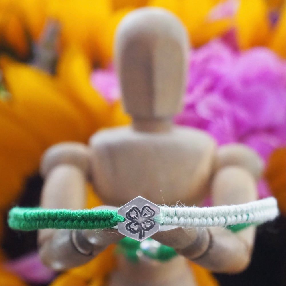 Fine silver charm with four leaf clover stamp on a green friendship bracelet