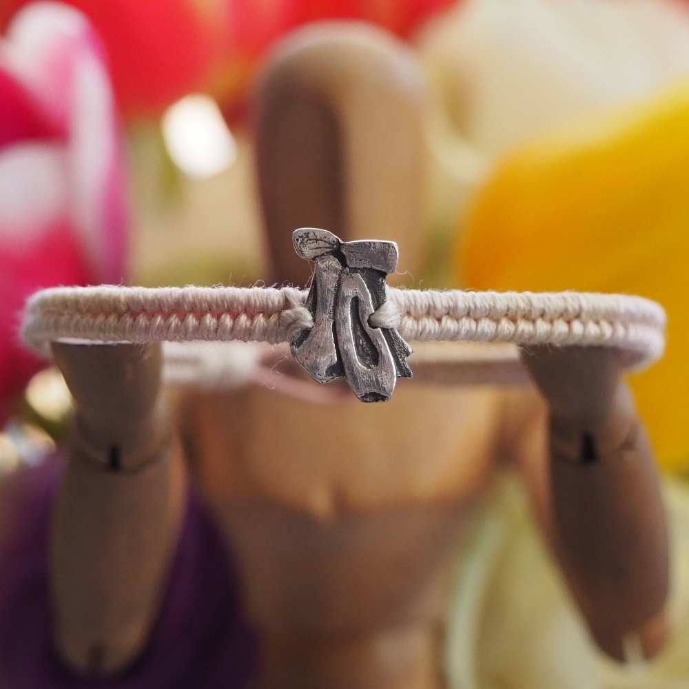 Fine small silver ballet shoes charm on a cream friendship bracelet