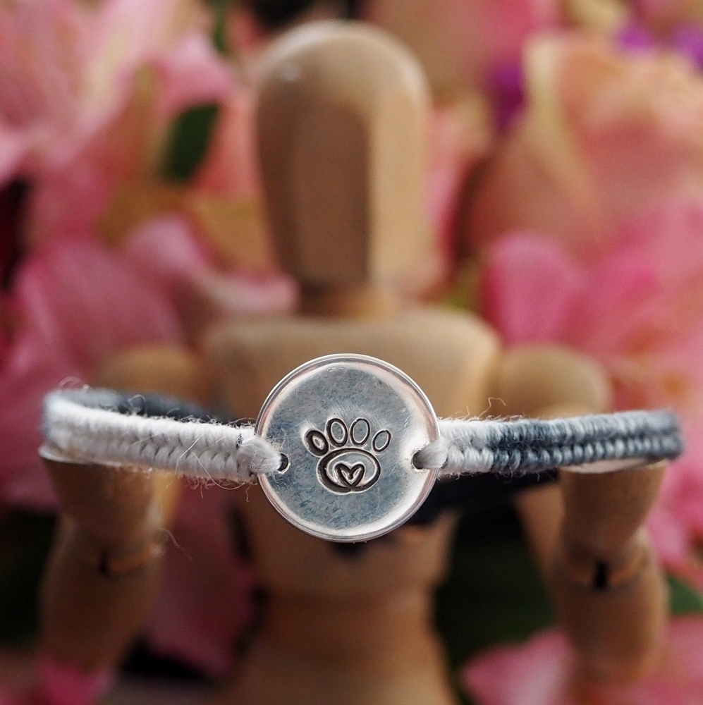 Fine silver disc charm with paw print stamp on a grey friendship bracelet