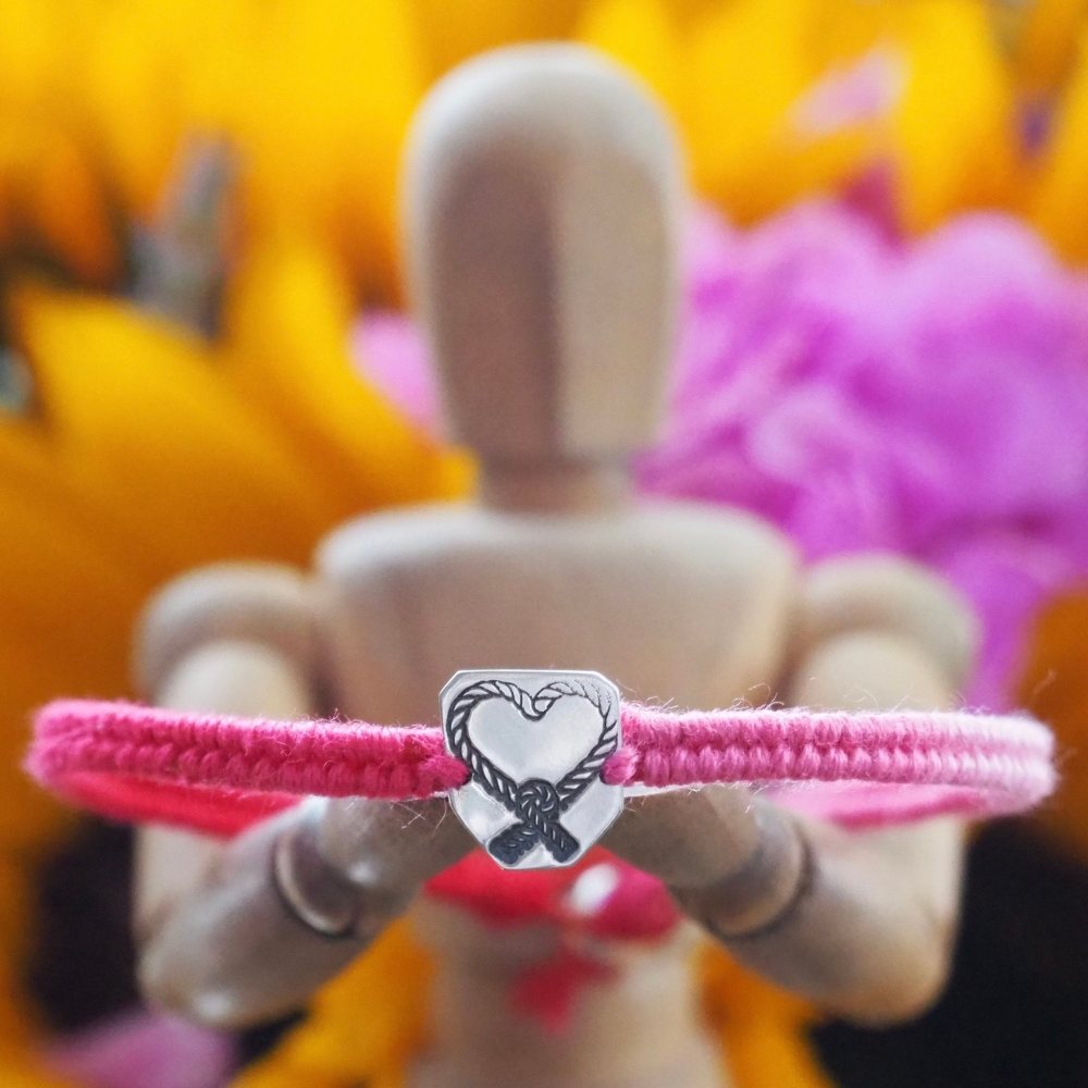 Fine silver charm with knotted heart stamp on a vivid pink friendship bracelet