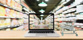 supermarket-aisle-blurred-background-with-laptop-computer-and-cart-on-wood-