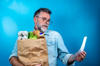 Shocked-mature-man-looking-at-store-receipt-after-shopping,-holding-a-paper