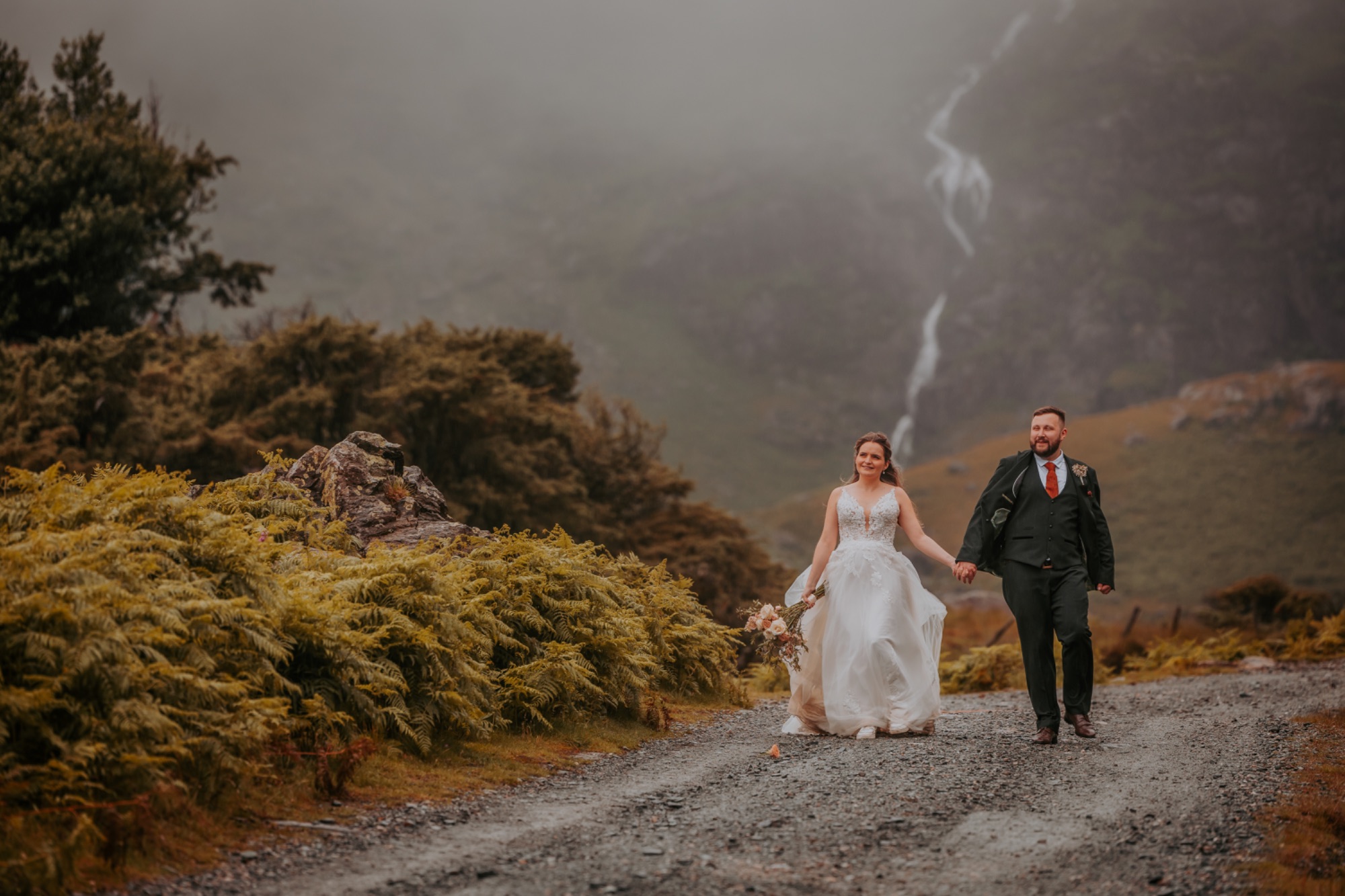 Coniston Coppermines, bride and groom walking away from waterfall as rain begins