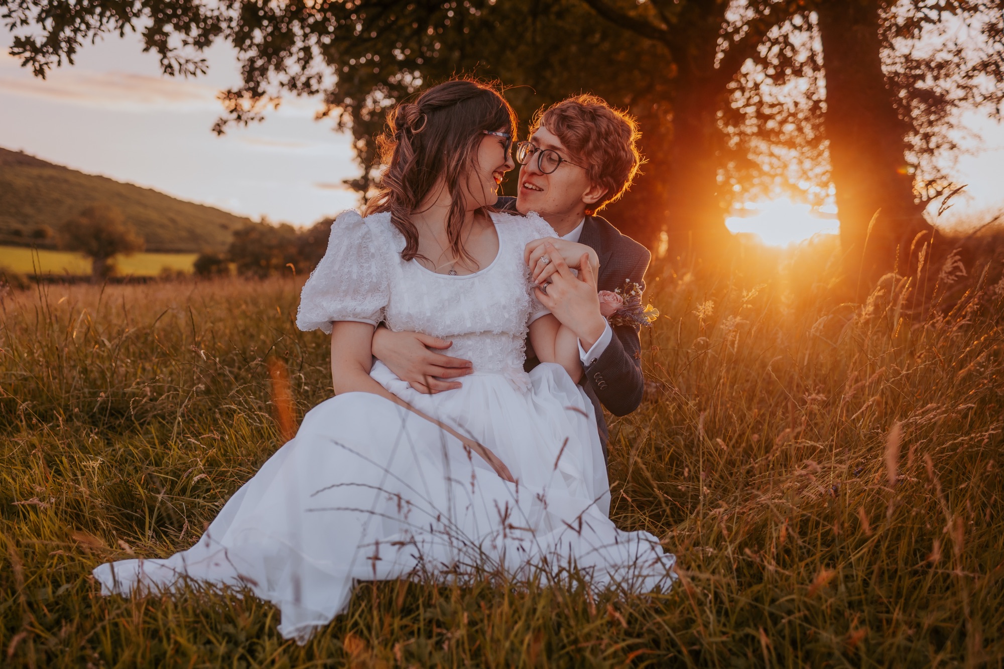 North Yorkshire bride and groom in long grass as sun sets through the trees on the horizon