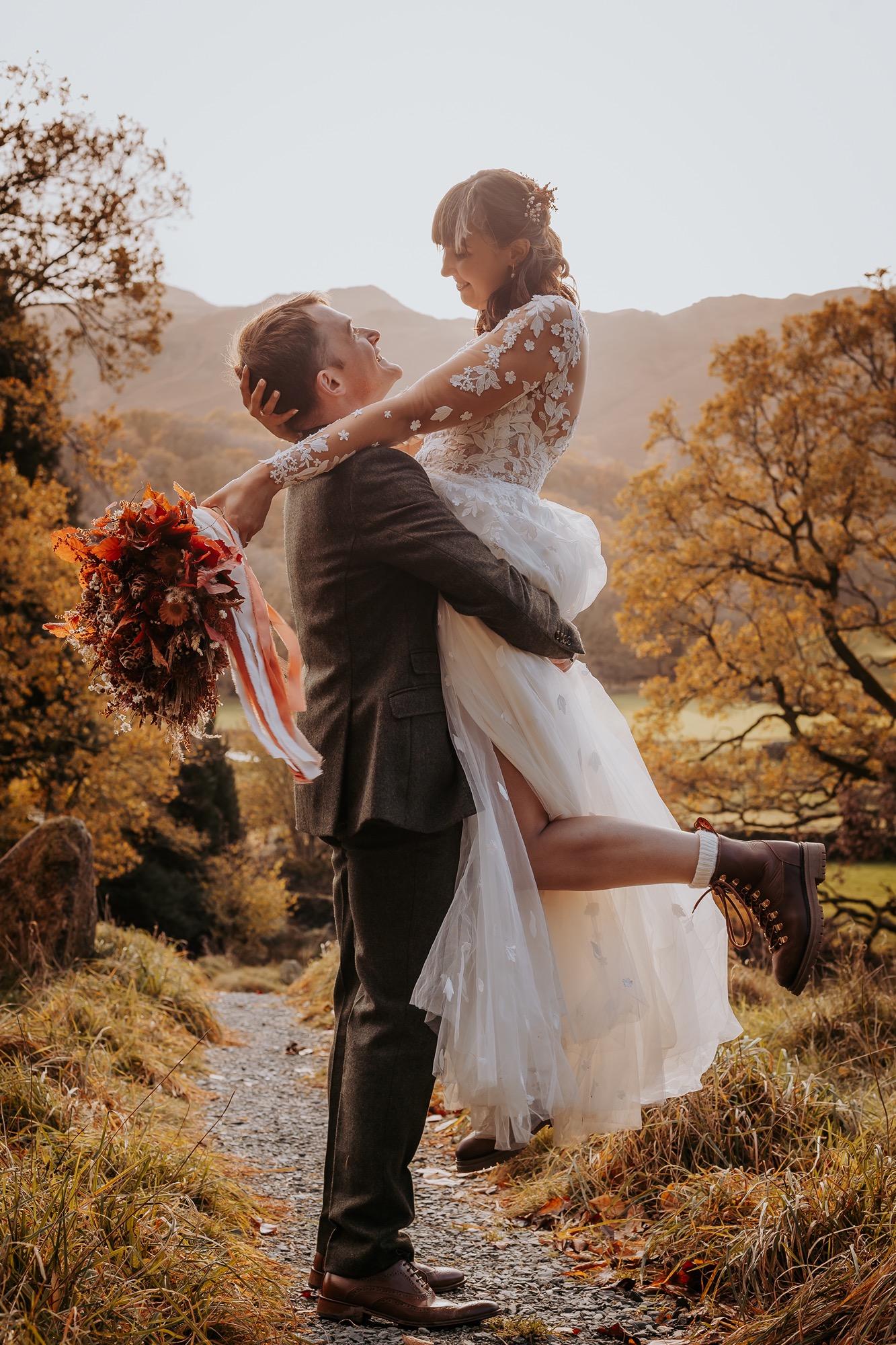 Groom lifting bride during Autumnal wedding on Lancrigg grounds with Lake District mountains in the background