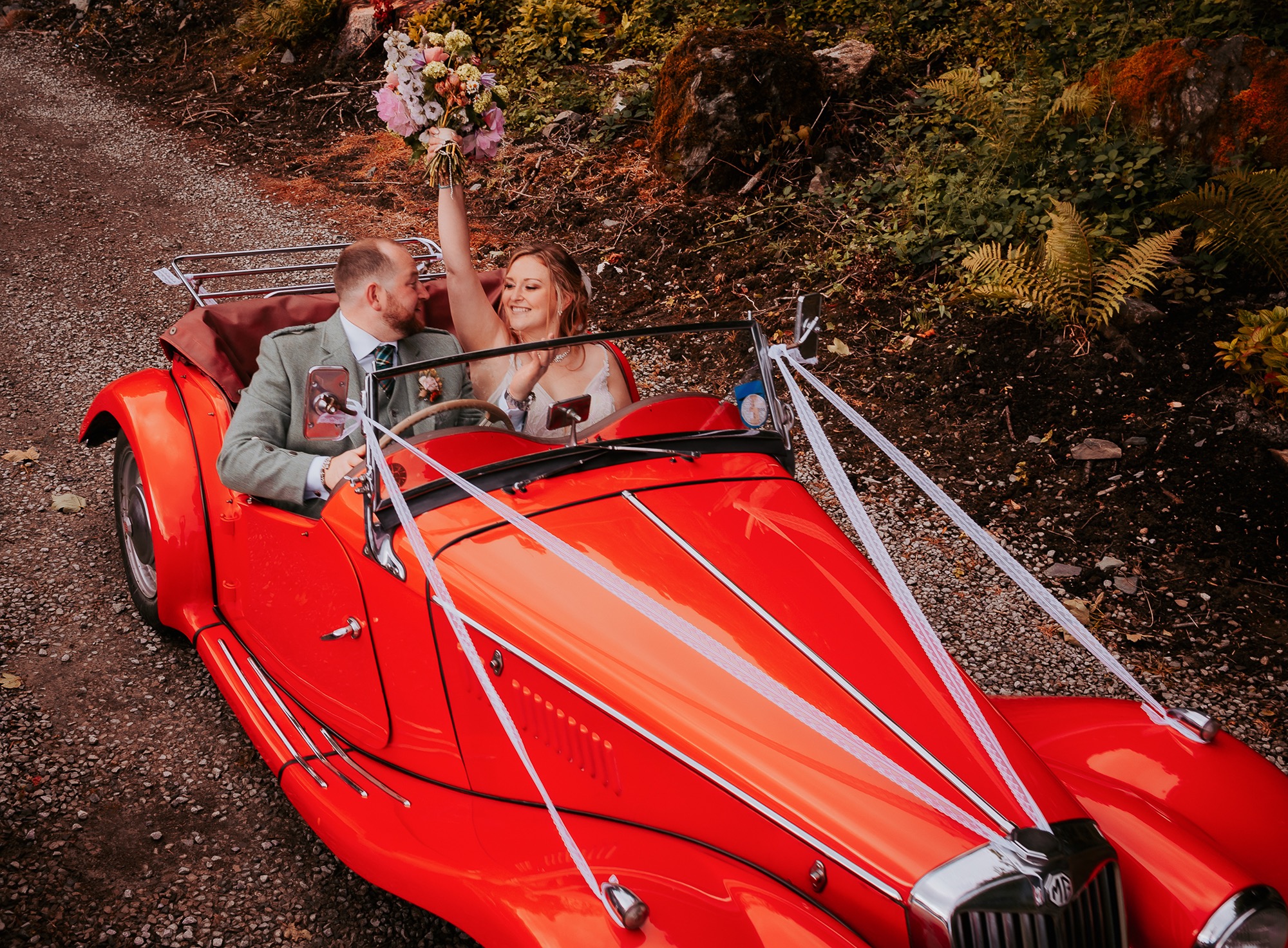 Bride and Groom enjoy a drive in red vintage car on wedding day