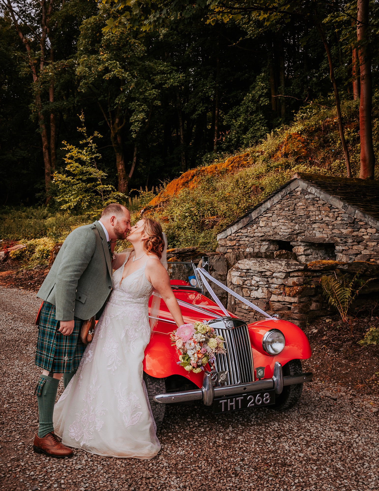 Wedding couple kiss over red vintage car in Town Head Estate grounds