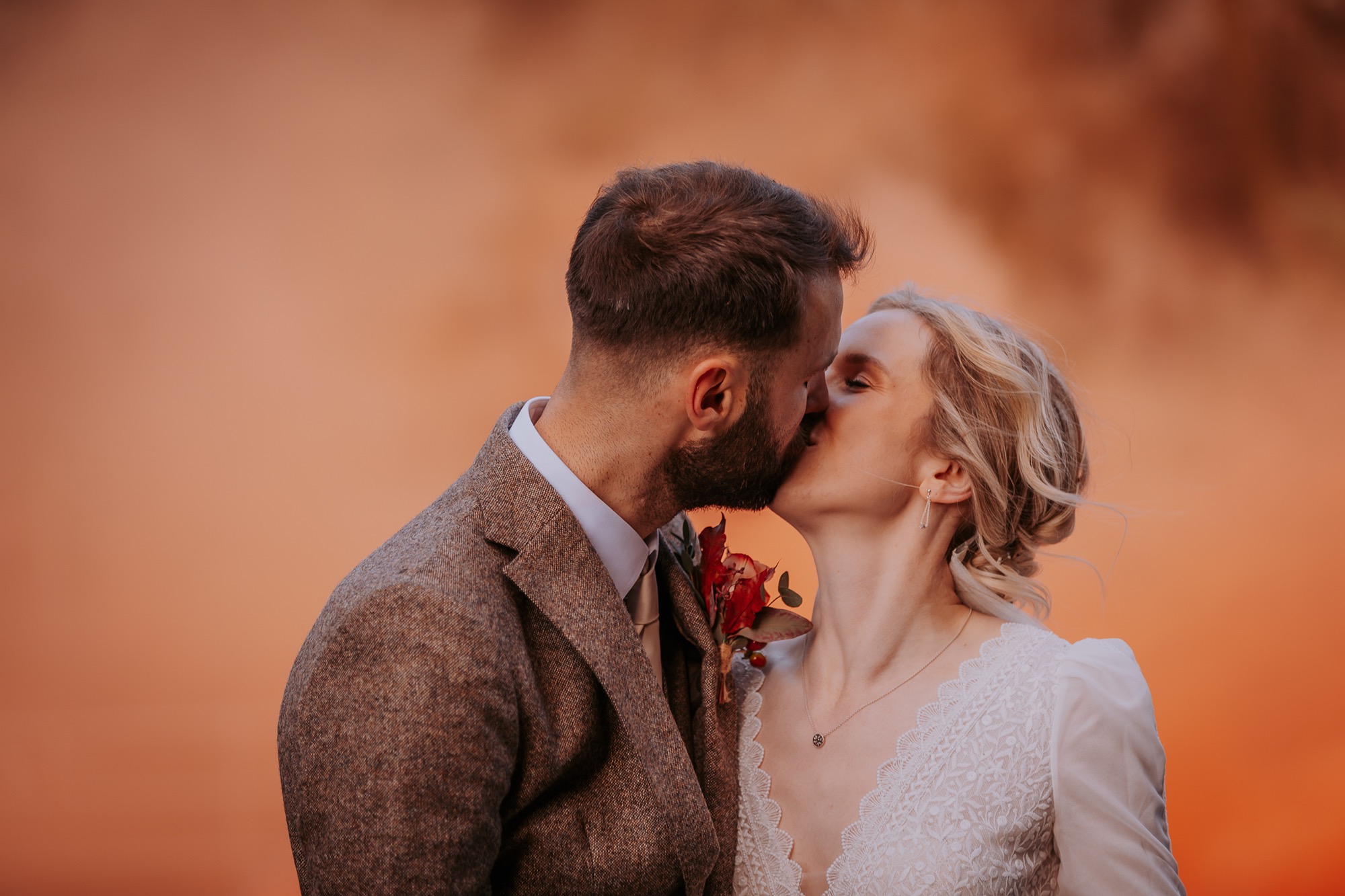 wedding couple exchange a kiss with orange smoke grenade surrounding them