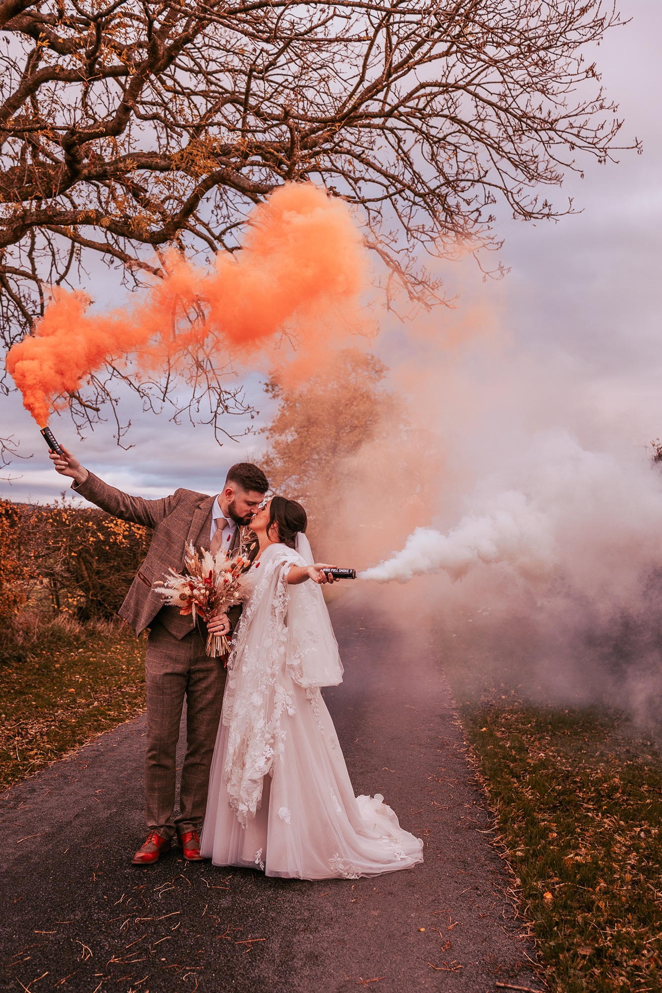 Bride and Groom on country road kissing with orange and white smoke grenades to celebrate their wedding