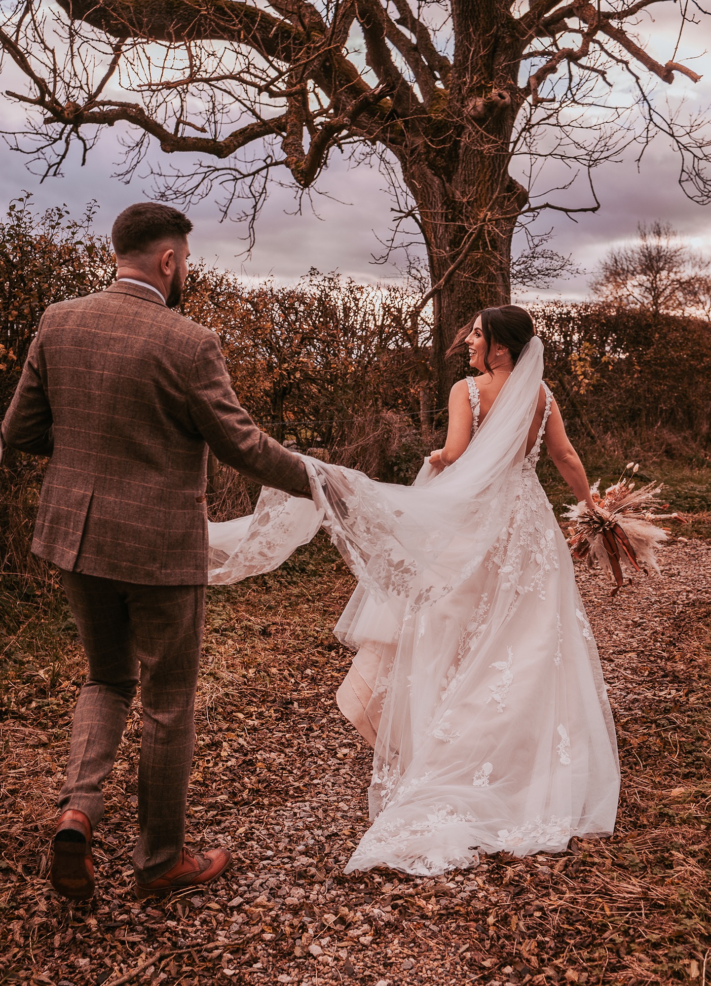 Bride looking back over her shoulder at her groom as they explore Eden Wedding Barns surroundings and countryside