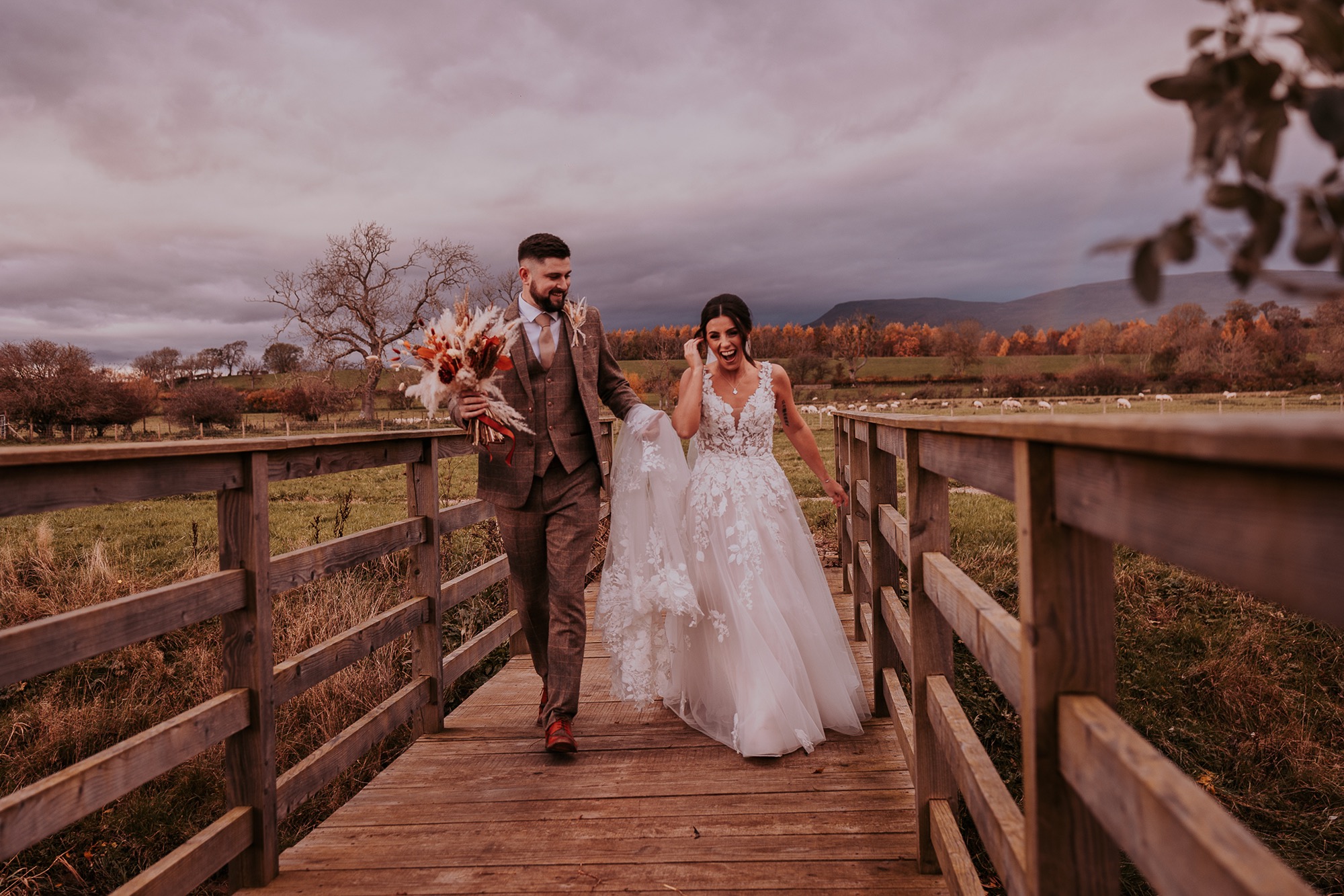 Mr & Mrs walk over small wooden bridge in Eden Wedding Barns countryside grounds