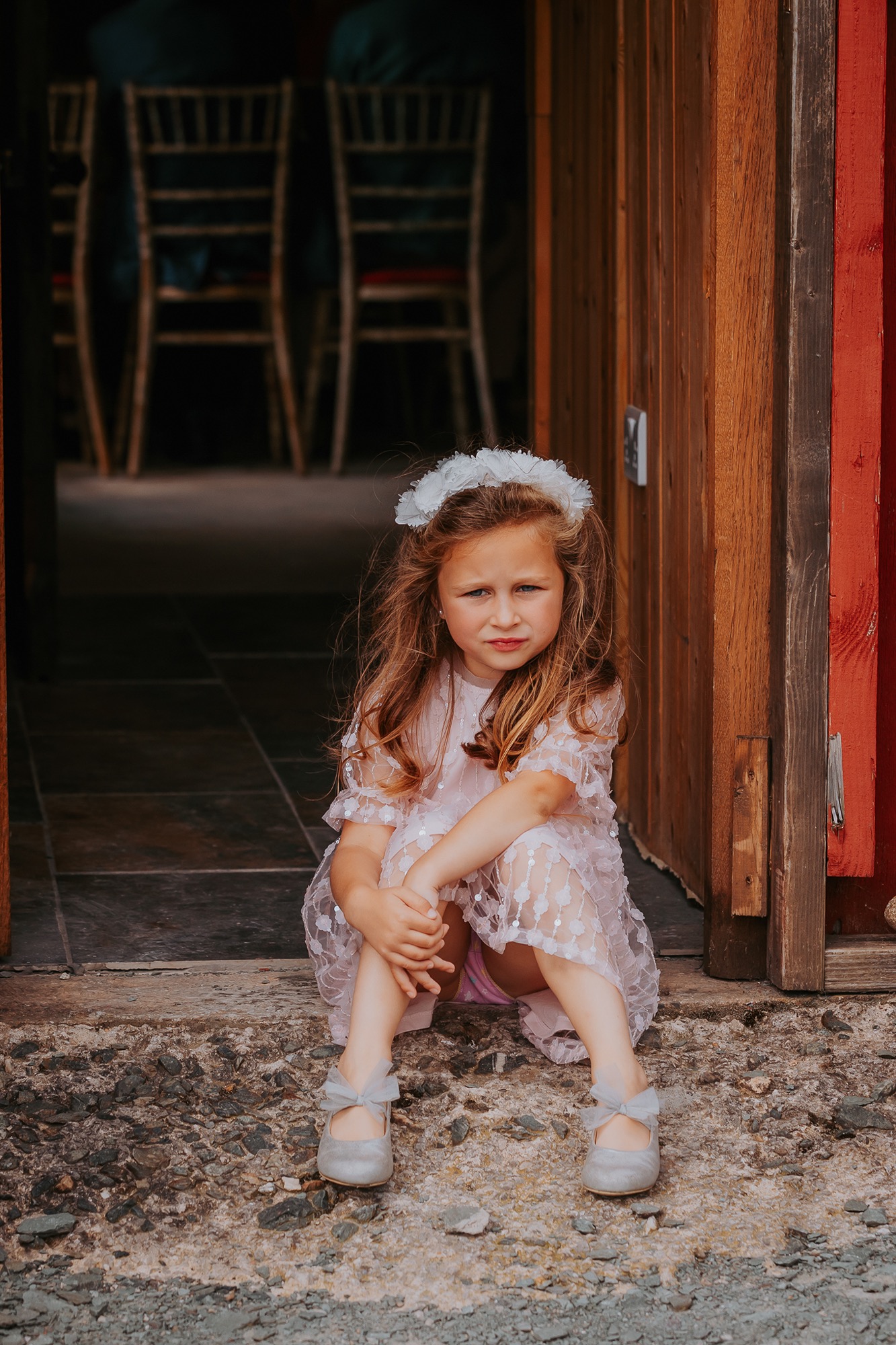 Flower girl waiting on doorstep on wedding barn at Coniston Coppermines