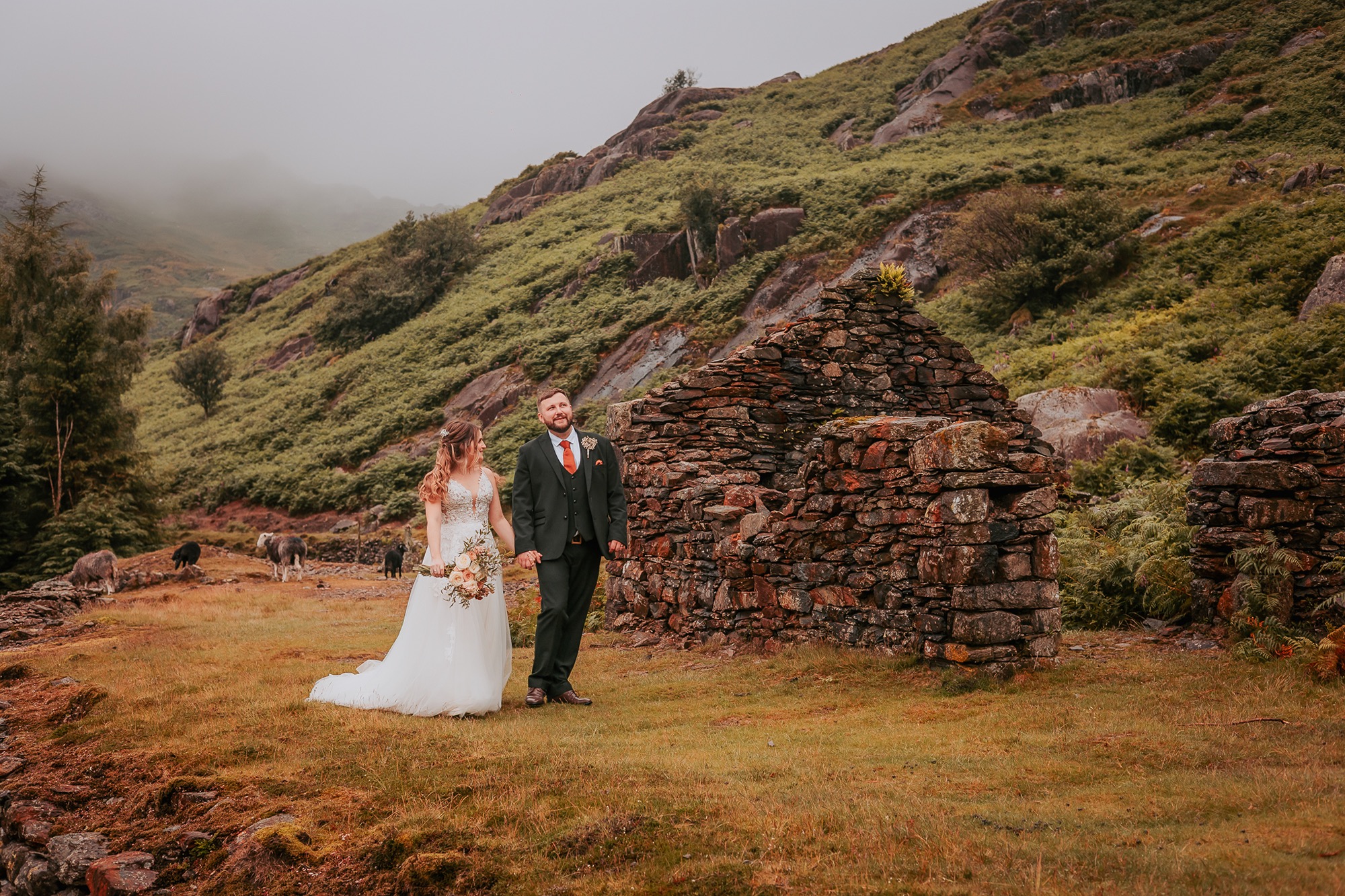 Bride and Groom walk near old shelter in the heart of the Lake District