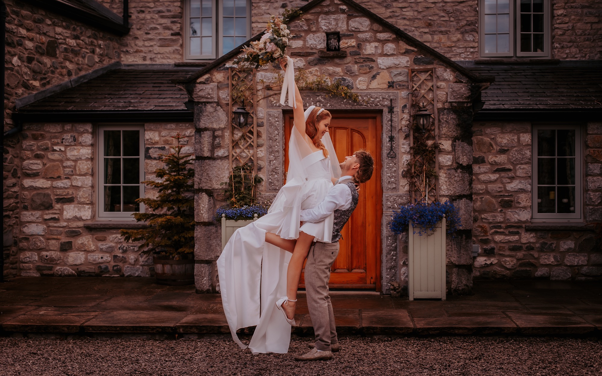 groom lifts bride is celebration outside farm house, North Yorkshire
