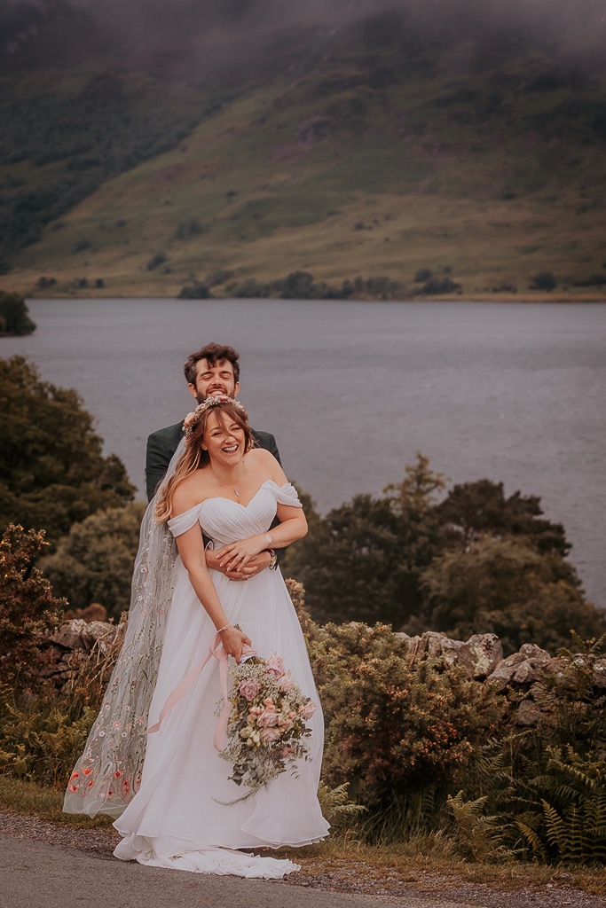 couple cuddle on the edge of Crummock water as Lake District wedding photographer, photographs them