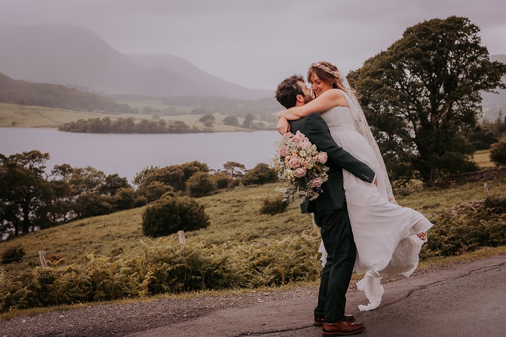 Groom lifts bride in joy after wedding ceremony on the shoes of Crummock water