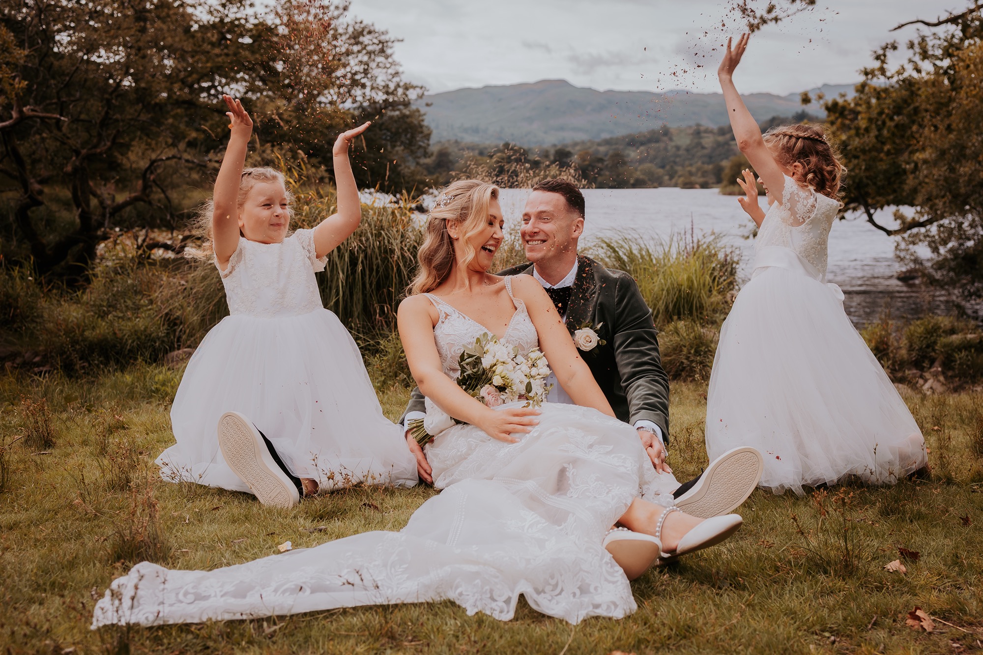 Bride and groom sit on the shores of Rydal water with their children after their elopement at Cote How, Ambleside