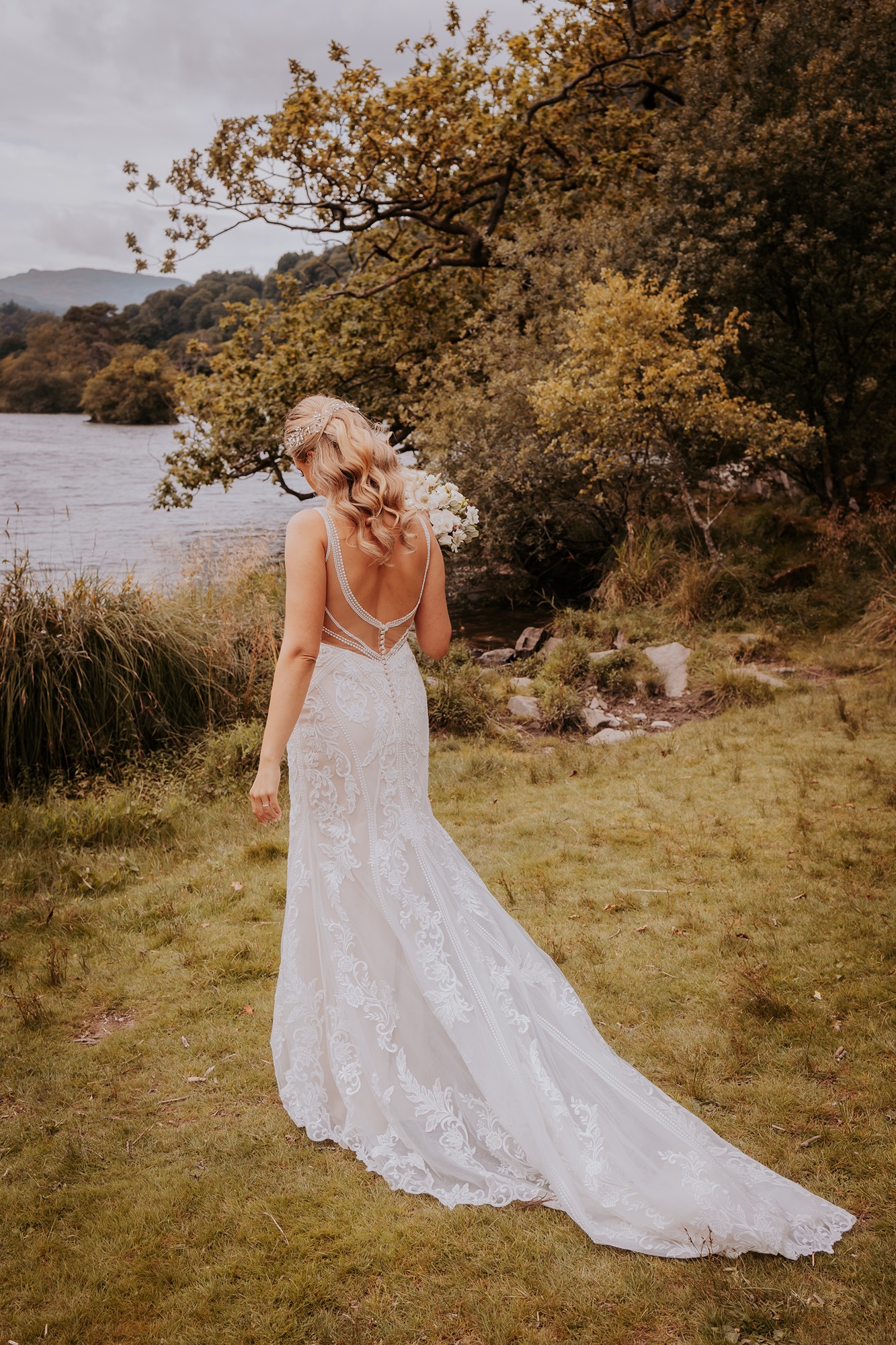 Bride walking towards the shores of Rydal water with wedding gown trailing behind