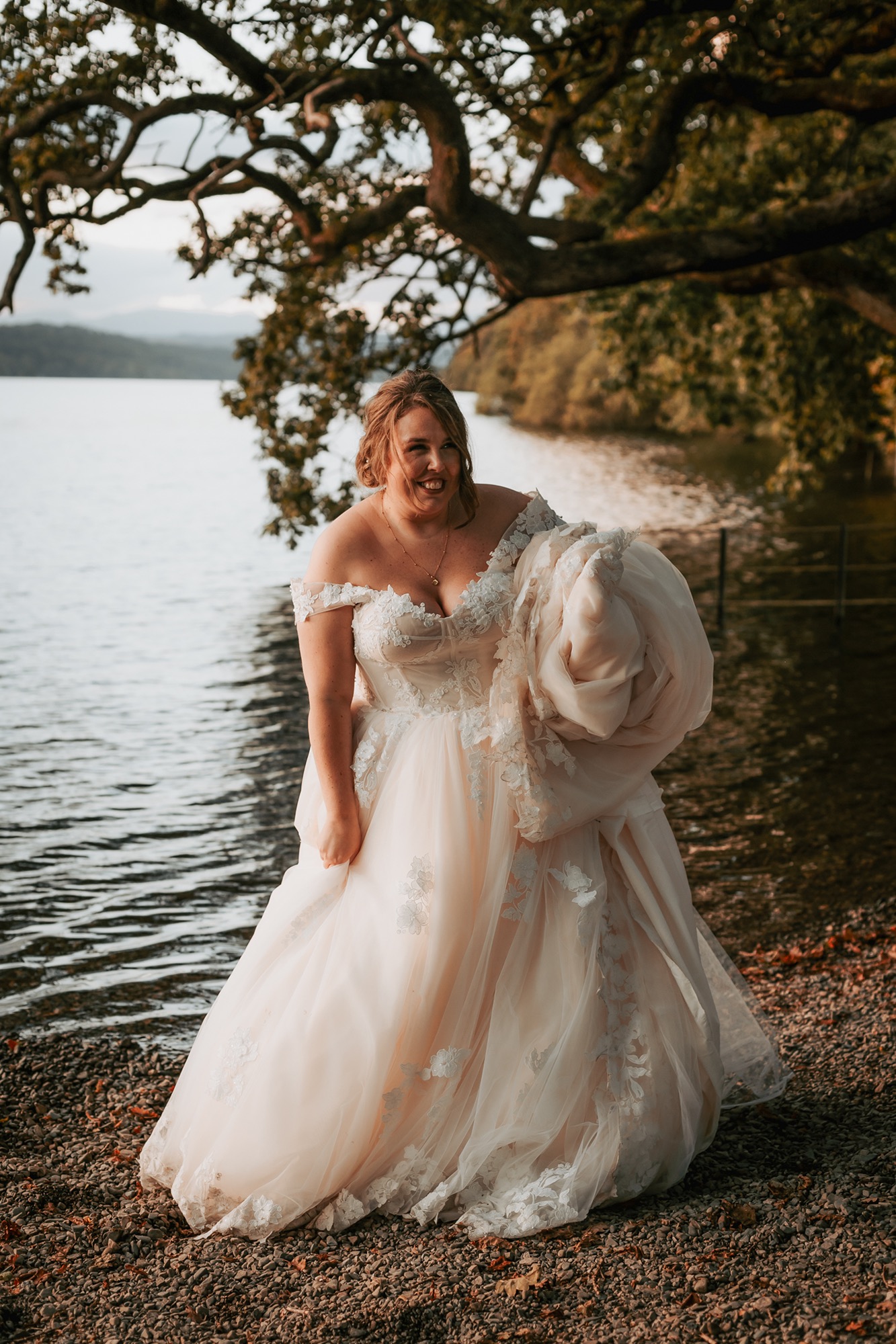 Bride carrying her dress near Windermere lake shores