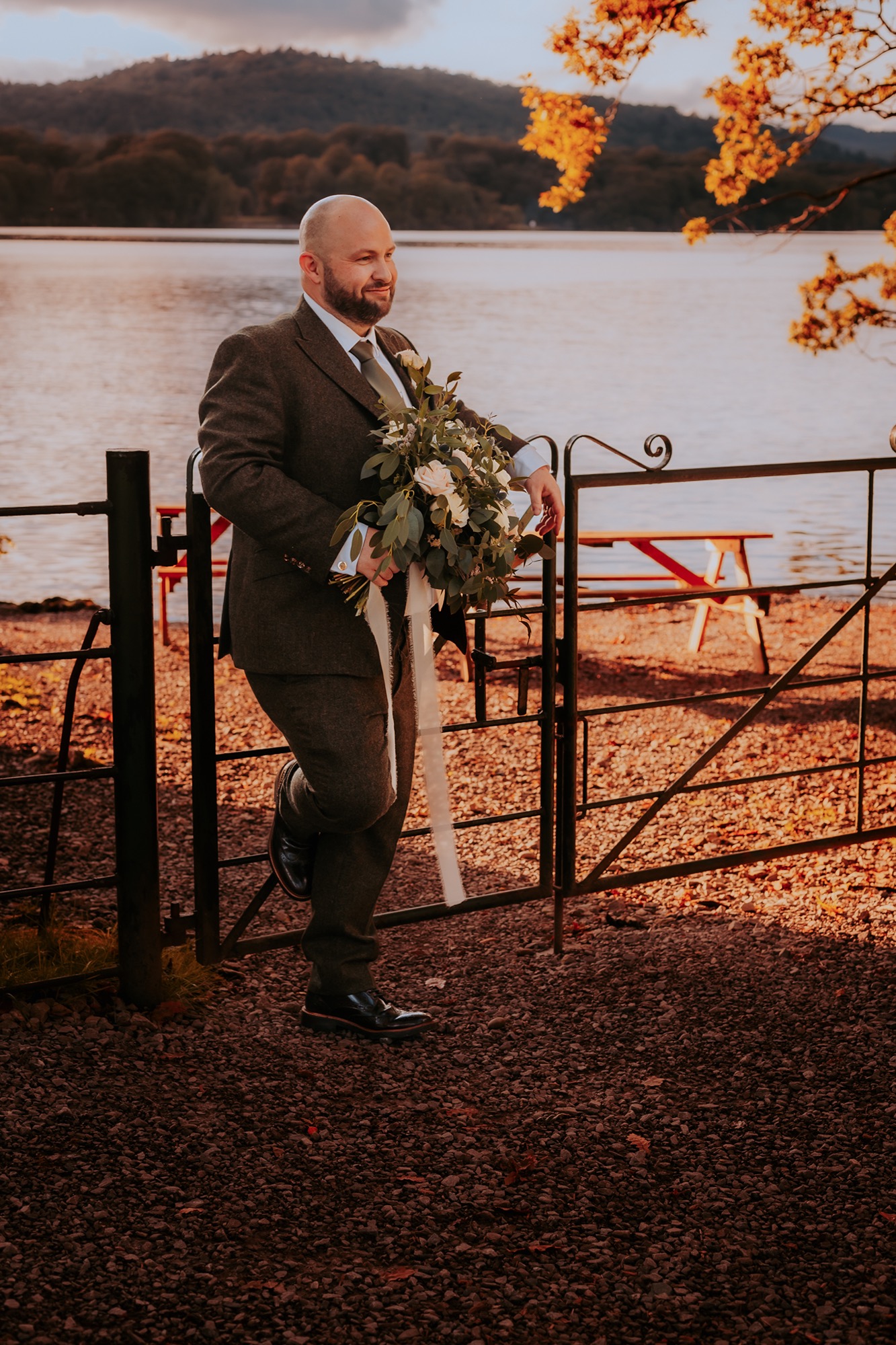 groom leans of metal gate in Windermere