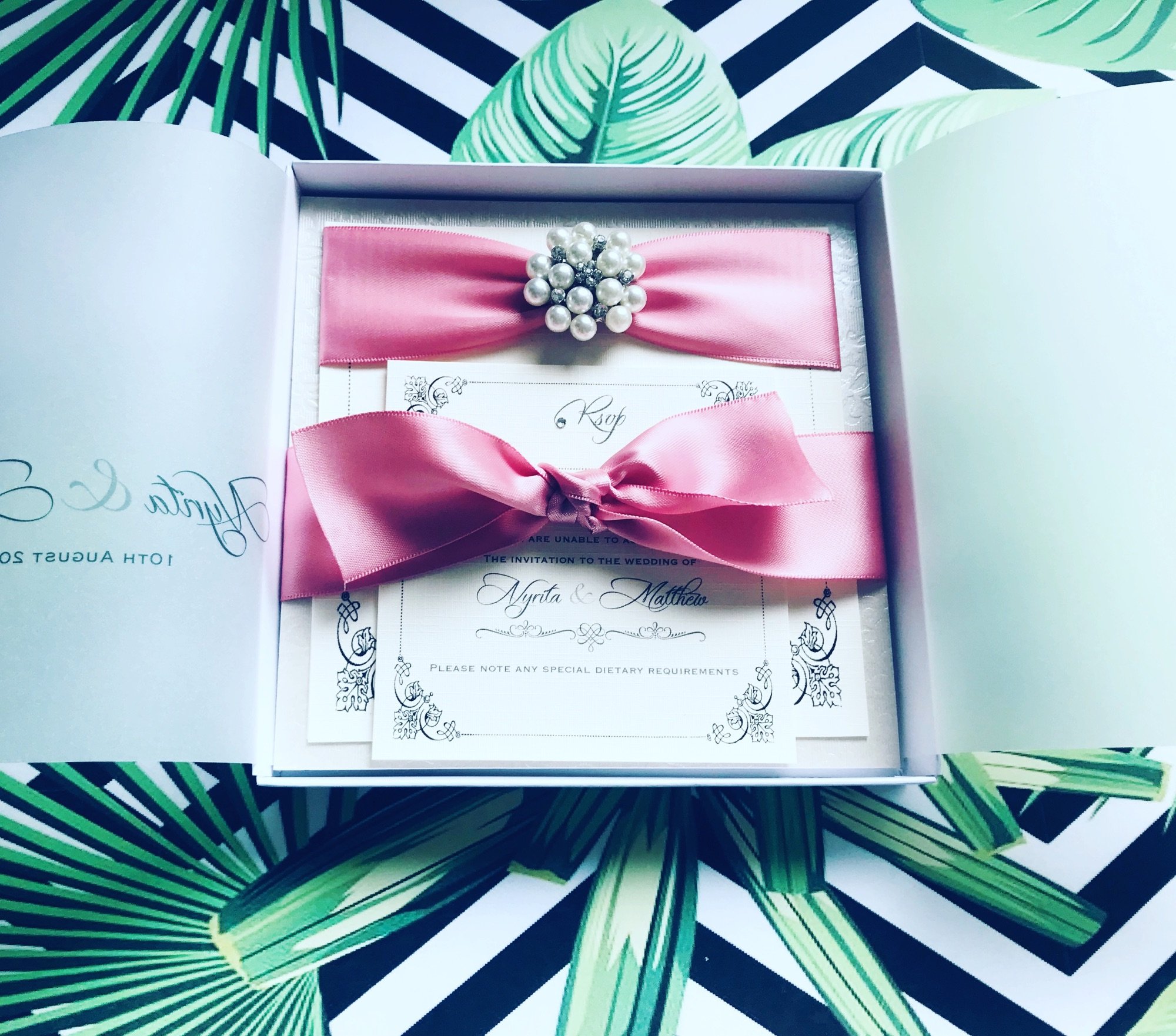 Boxed wedding invitation with dusky pink ribbon and a pearl crystal brooch with rsvp and additional inserts