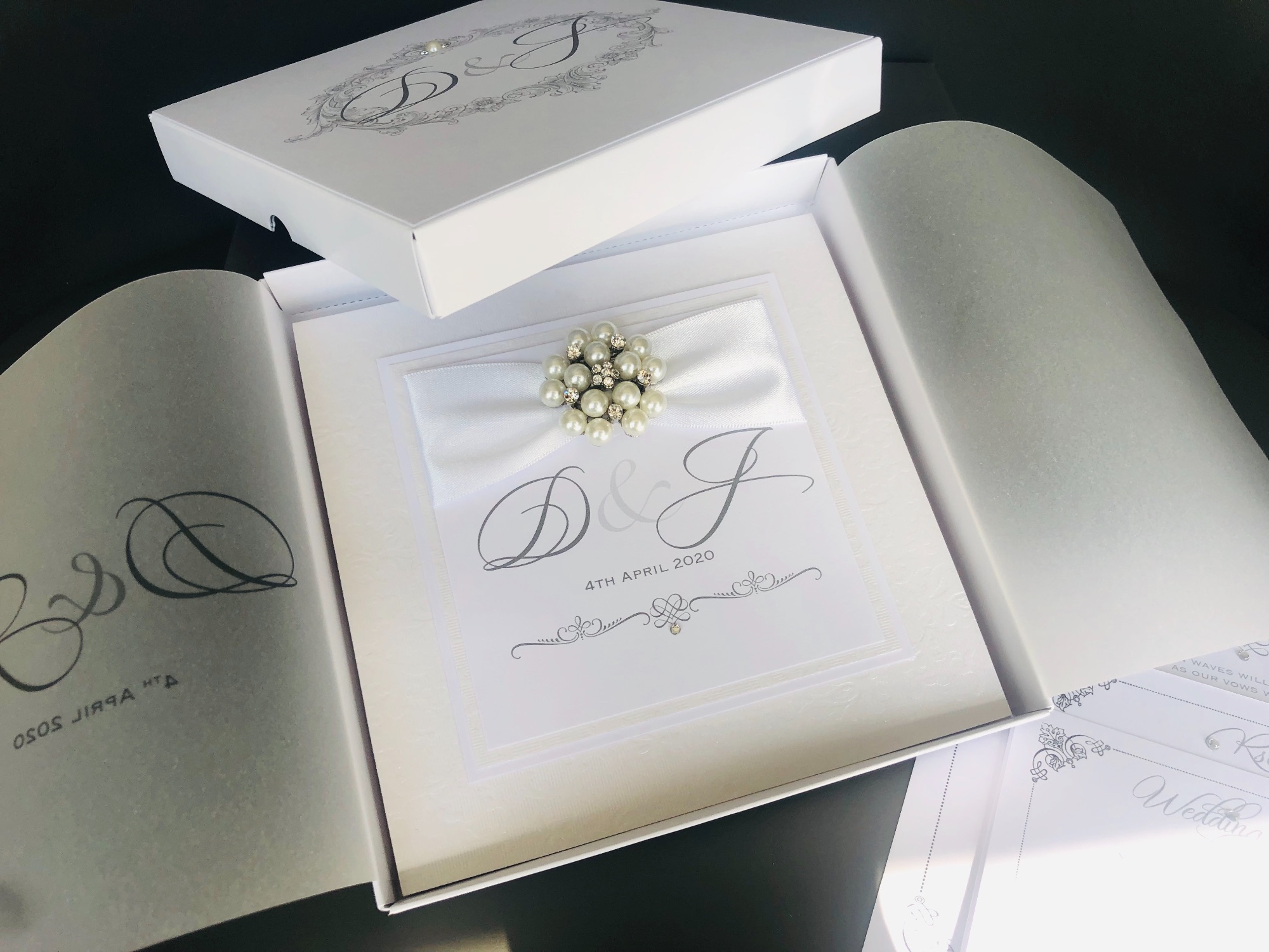 White monogrammed boxed wedding invitations with pearl brooch