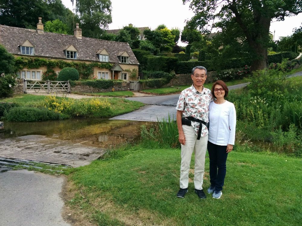 Japanese man and woman standing by a river in Cotswolds.house.river.countryside.sightseeing