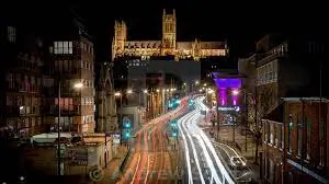 Night-time view of Lincoln city centre with Lincoln Cathedral lit up and traffic light trails along the main road