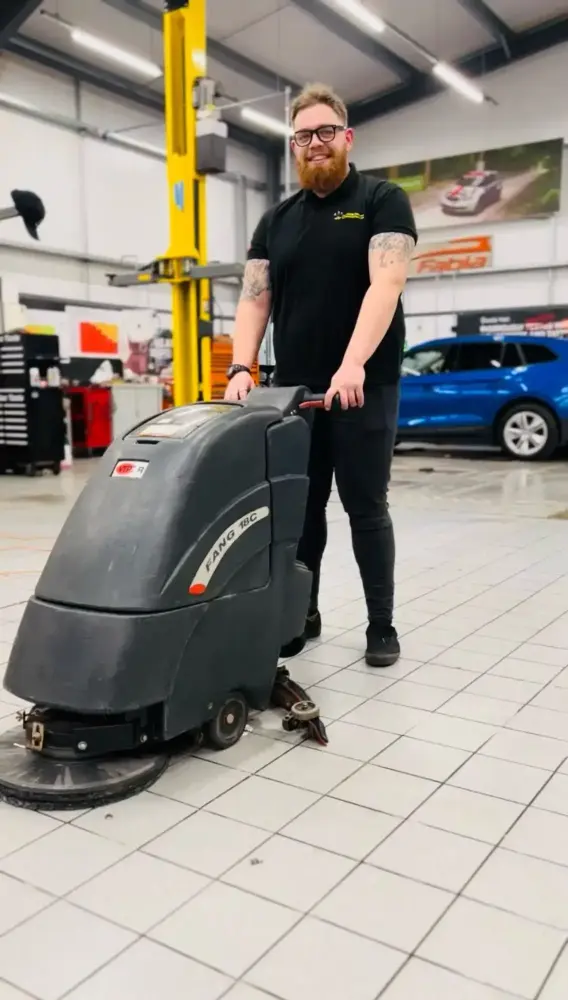 Uniformed staff using machine to clean Gainsborough car dealership workshop floor efficiently