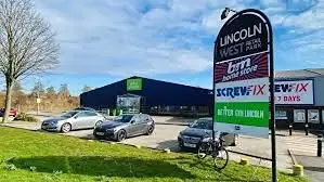 View of Lincoln West Retail Park showing Screwfix and B&M Home Store with parked cars and clean, well-maintained surroundings.