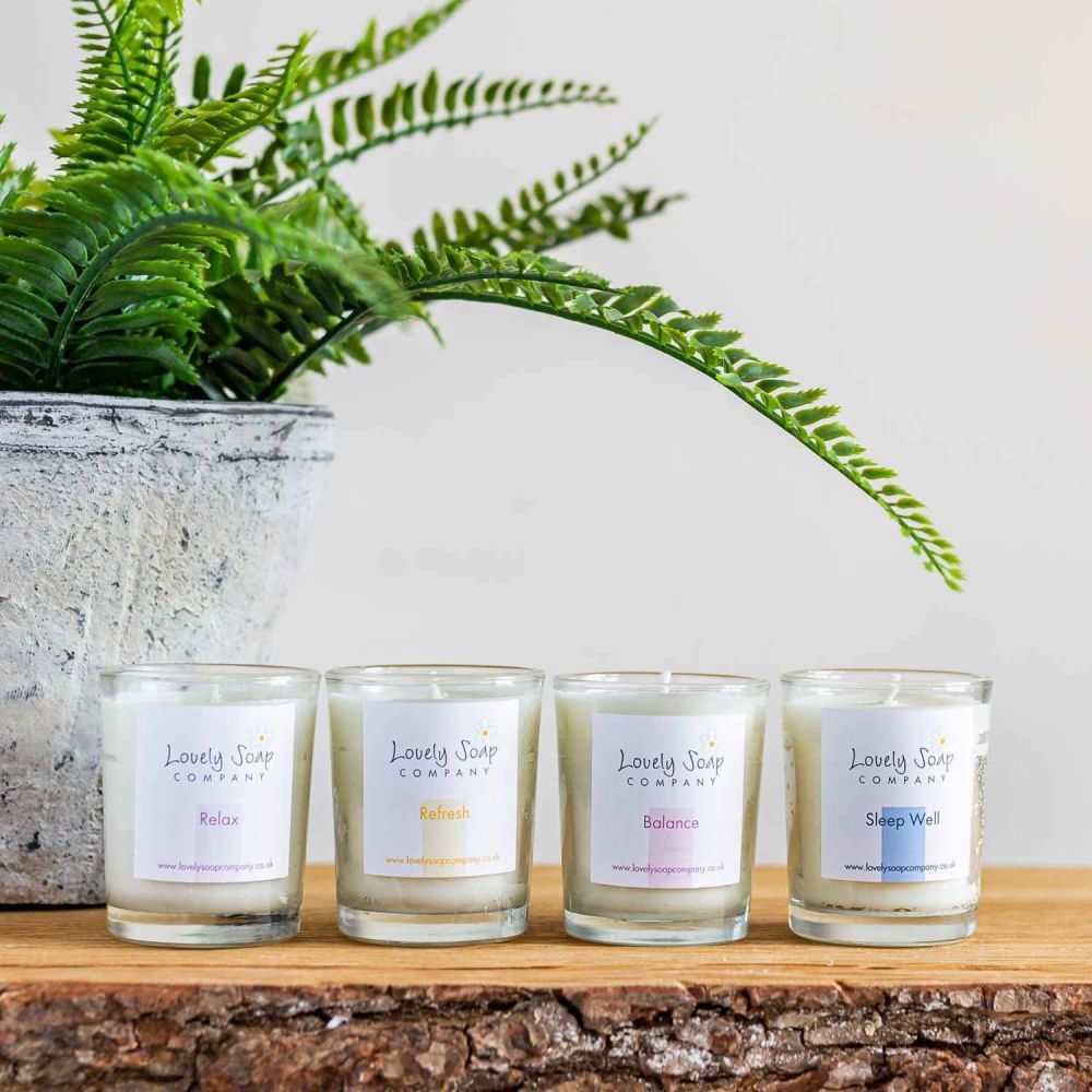 4 essential oil candles in a line with a green fern in the background Lovely Soap Co