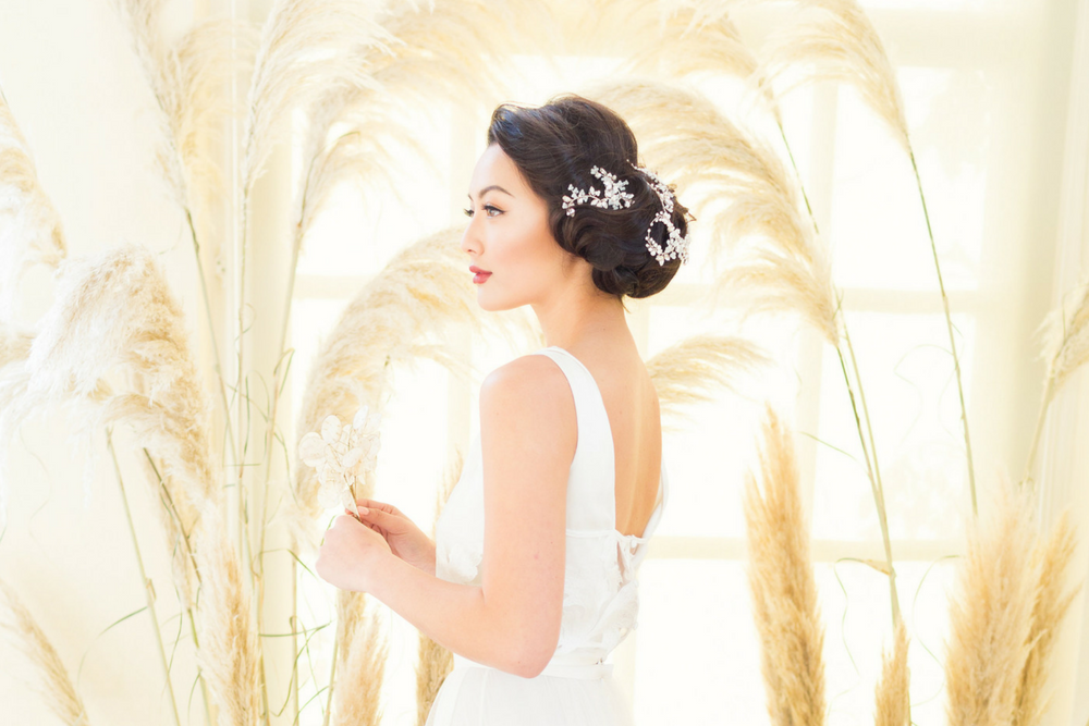 A bridal model stands in front of dried pampas grass and wears an elegant crystal headpiece in her hair