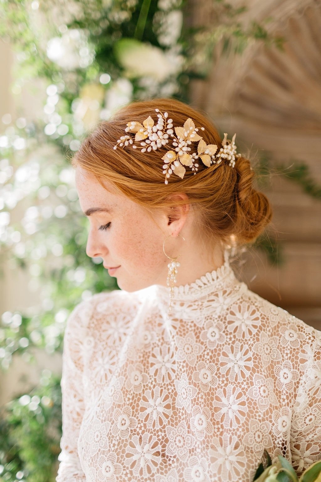 A bride with red hair worn in a low bun wears a pale gold leaf and freshwater pearls wedding headpiece made by Clare Lloyd