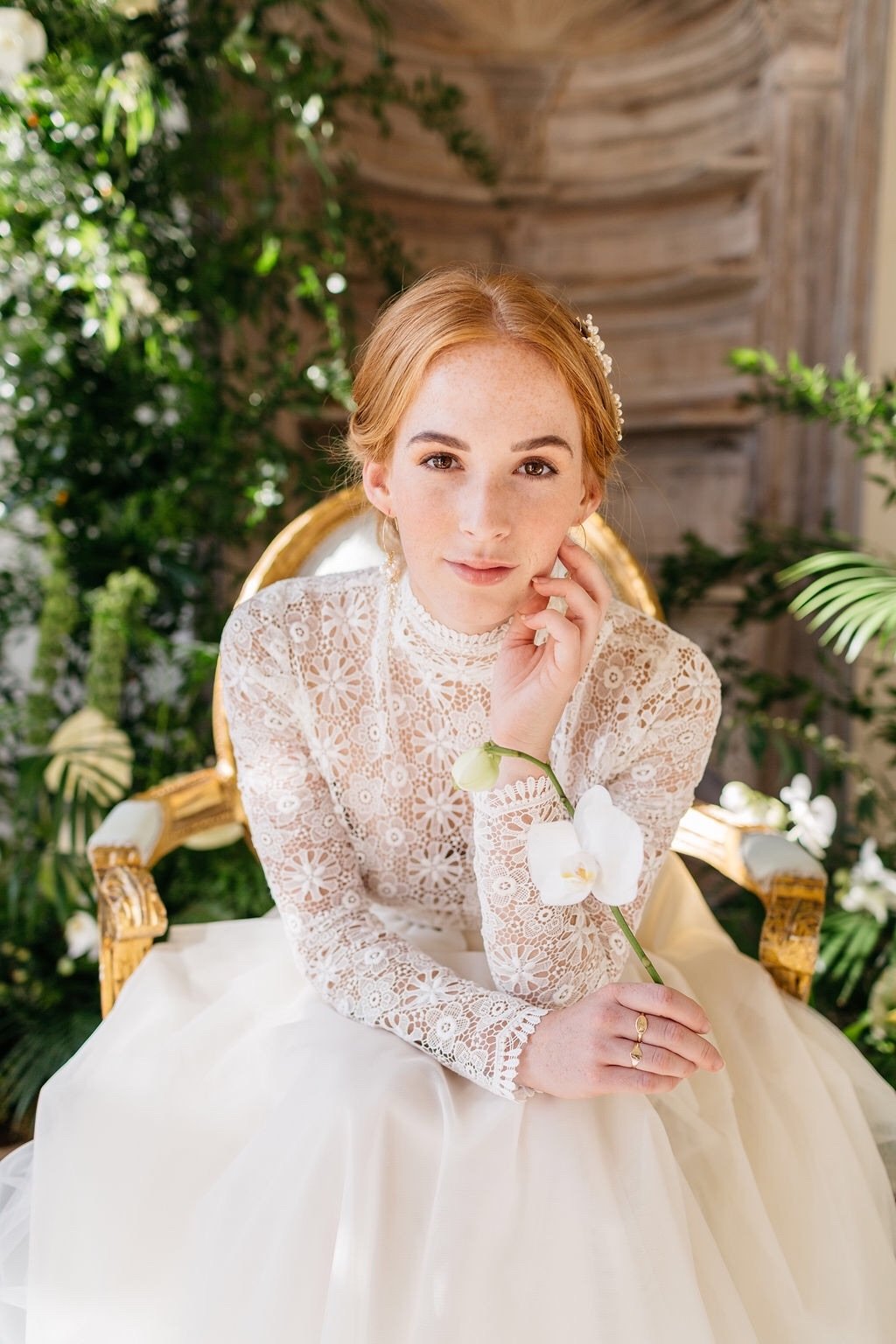 A red haired model wearing a lace wedding dress holding an orchid flower