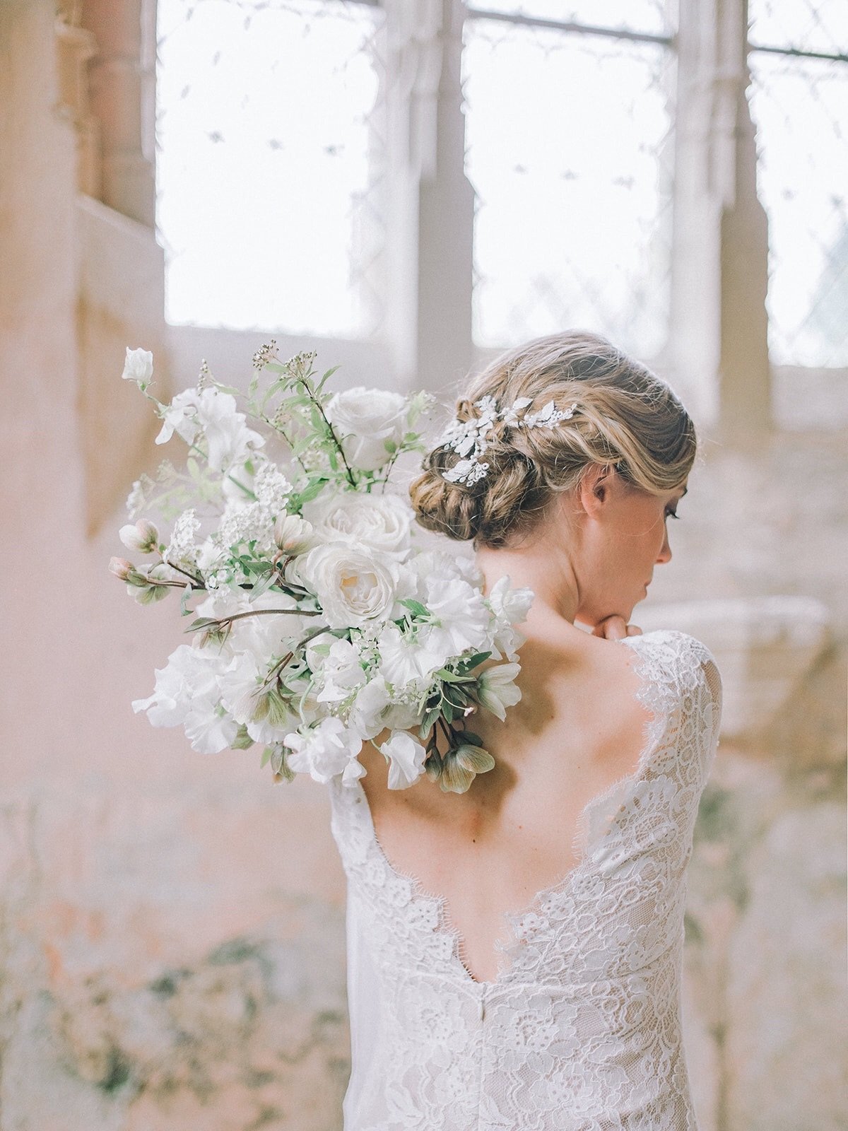 A bridal model wears a Claire Pettibone dress and hold a bouquet of white flowers over her shoulder