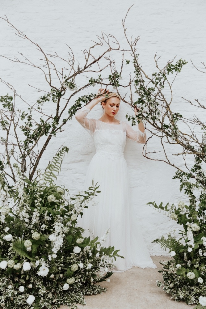 A bridal model wears a handmade couture wedding dress and stands under an arch of blackthorn blossom