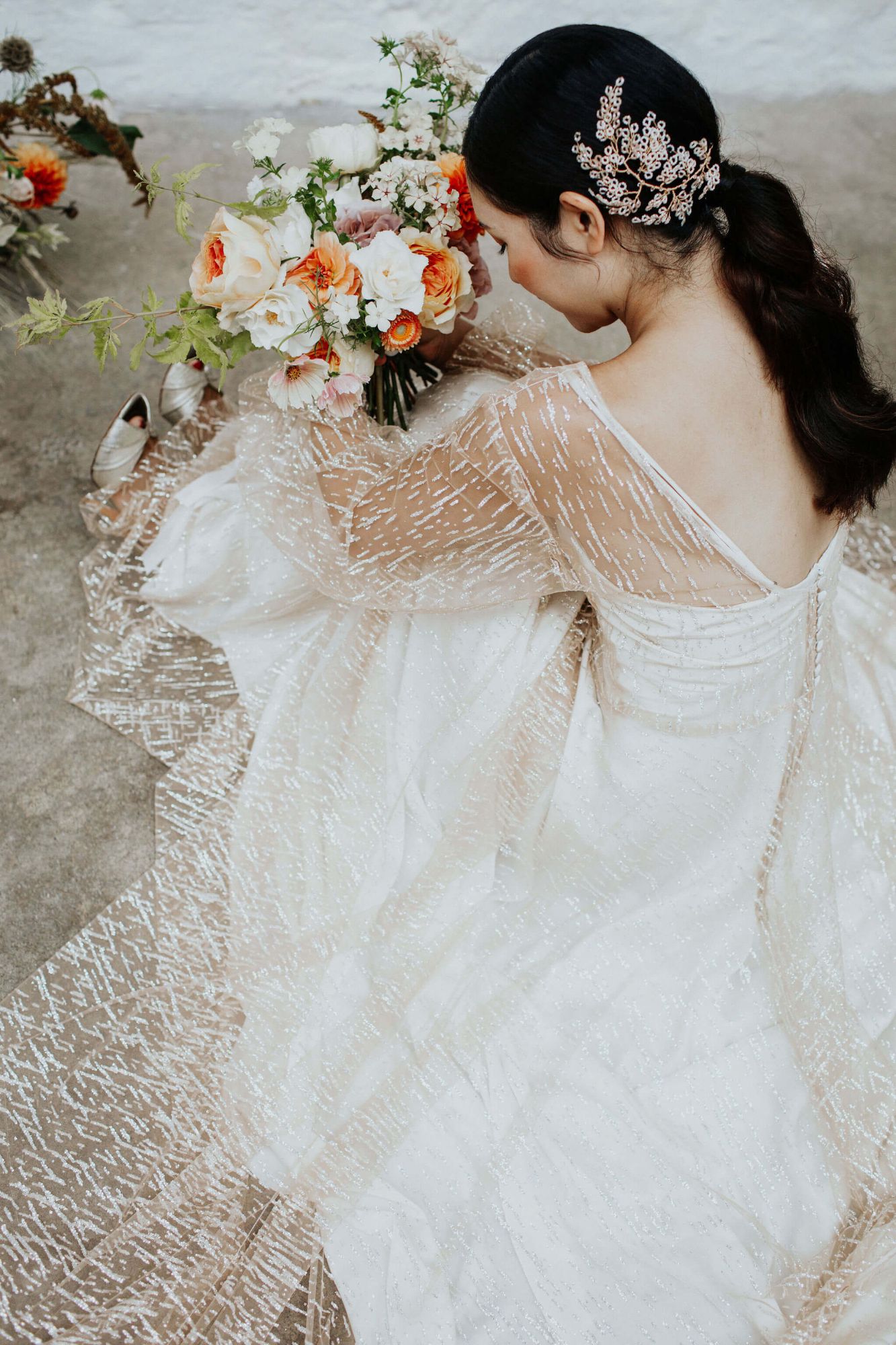 A model is sitting on the floor wearng a gold glittery wedding gown by Rachel Burgess Bridal Boutique and a delicate blossom headpiece by Clare Lloyd Accessories