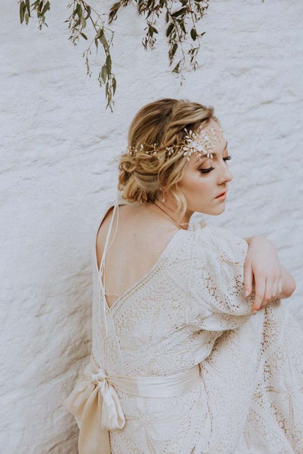 A model wearing an antique lace wedding dress is sitting on a bench she is wearing a mother of pearl 1920s style wedding headpiece