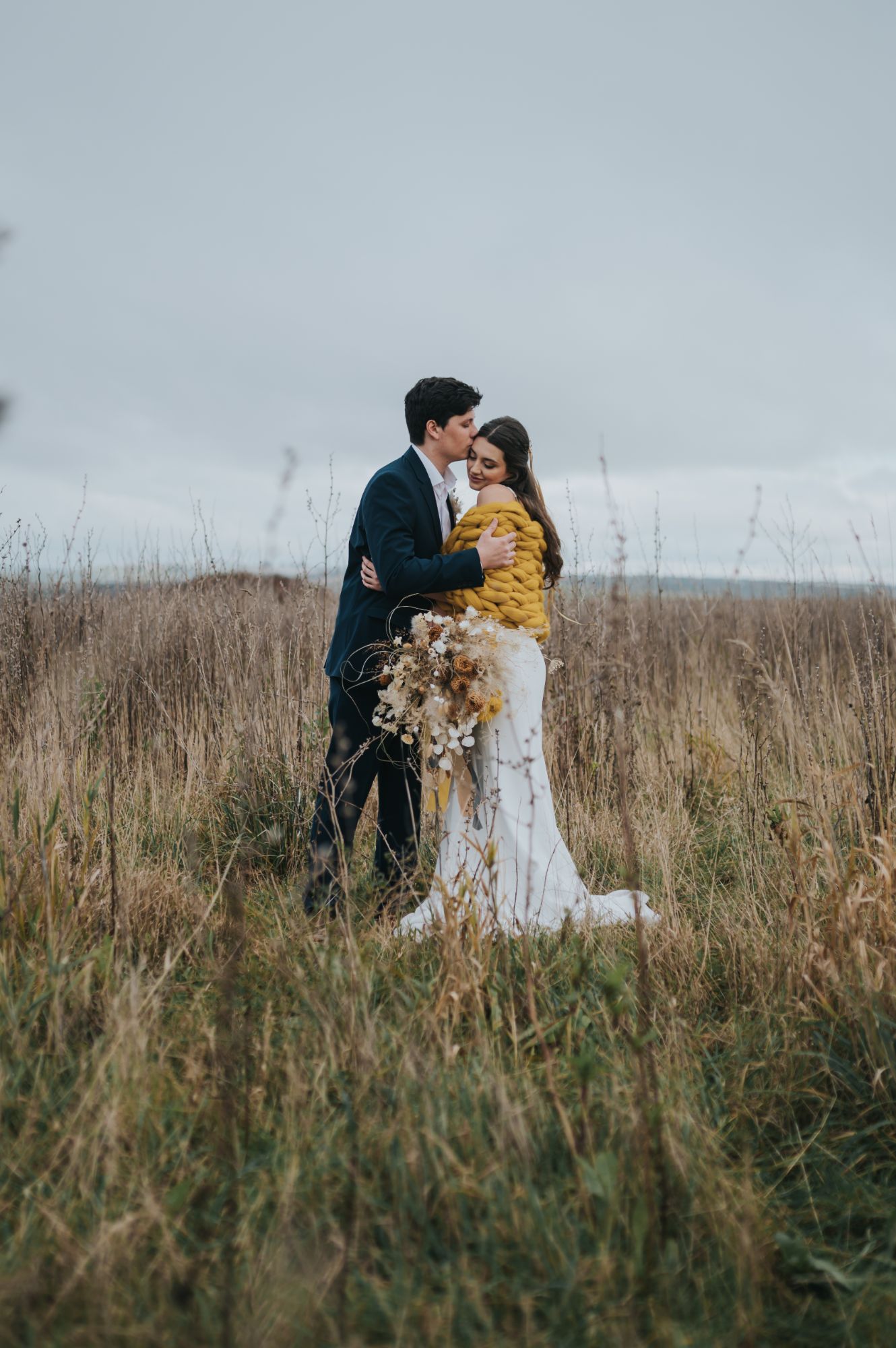 A bride and groom stand in a field in the winter 