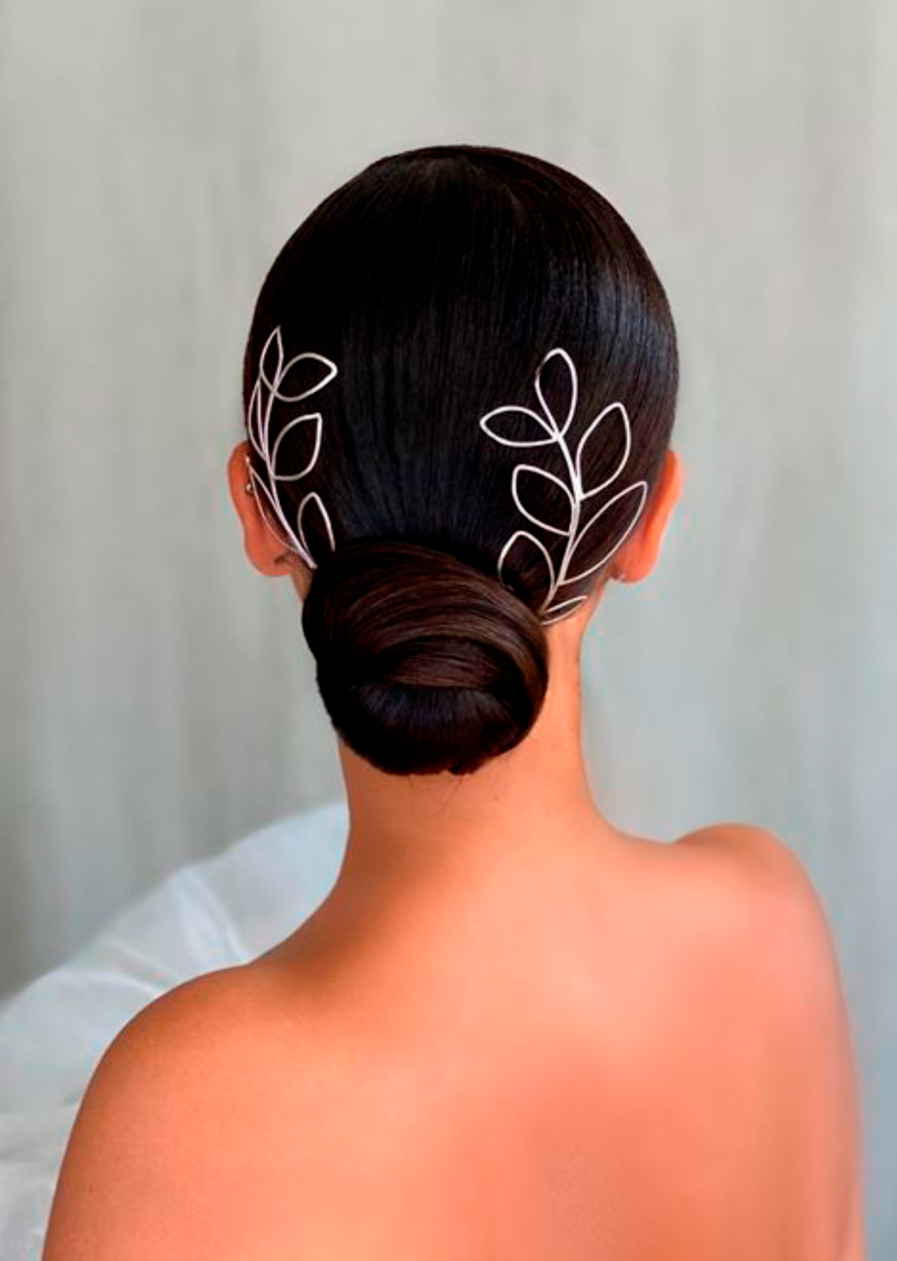 A bride with a sleek low bun wears two silver outline leaf headpieces in her hair styled by Kasia Fortuna