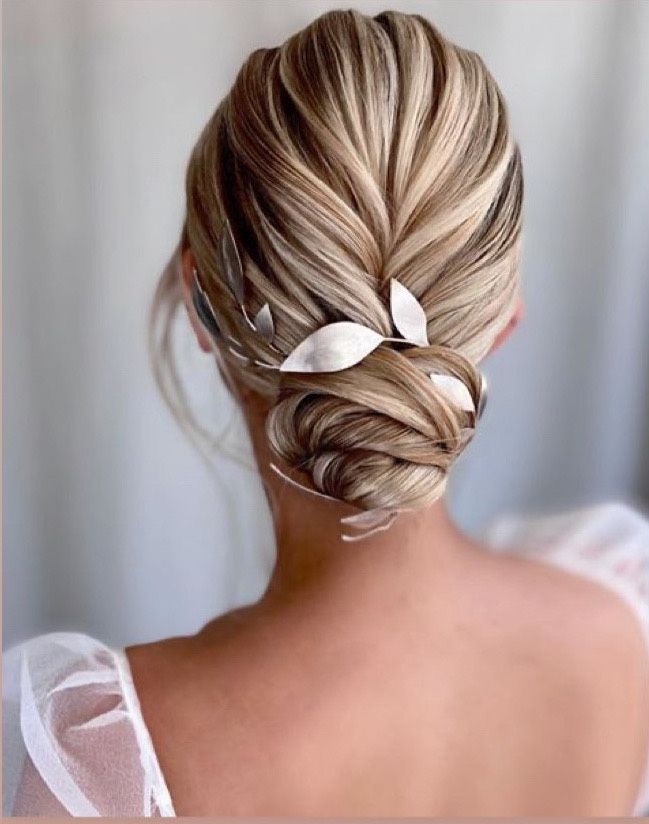 A blonde haired bride wears her hair in a low twisted bun with a silver leaf headpiece wrapped around the bun styled by Kasia Fortuna