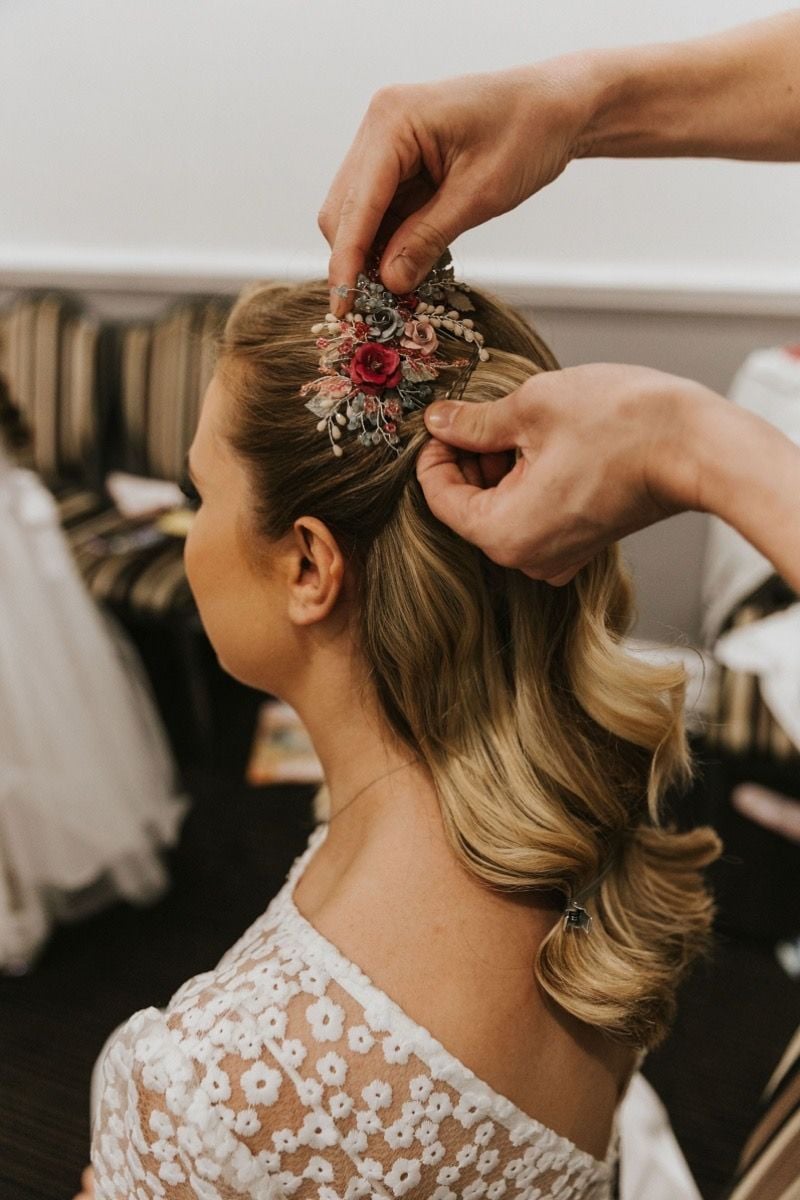 Hair stylist places colourful floral hair comb in the side of brides hollywood waves hair