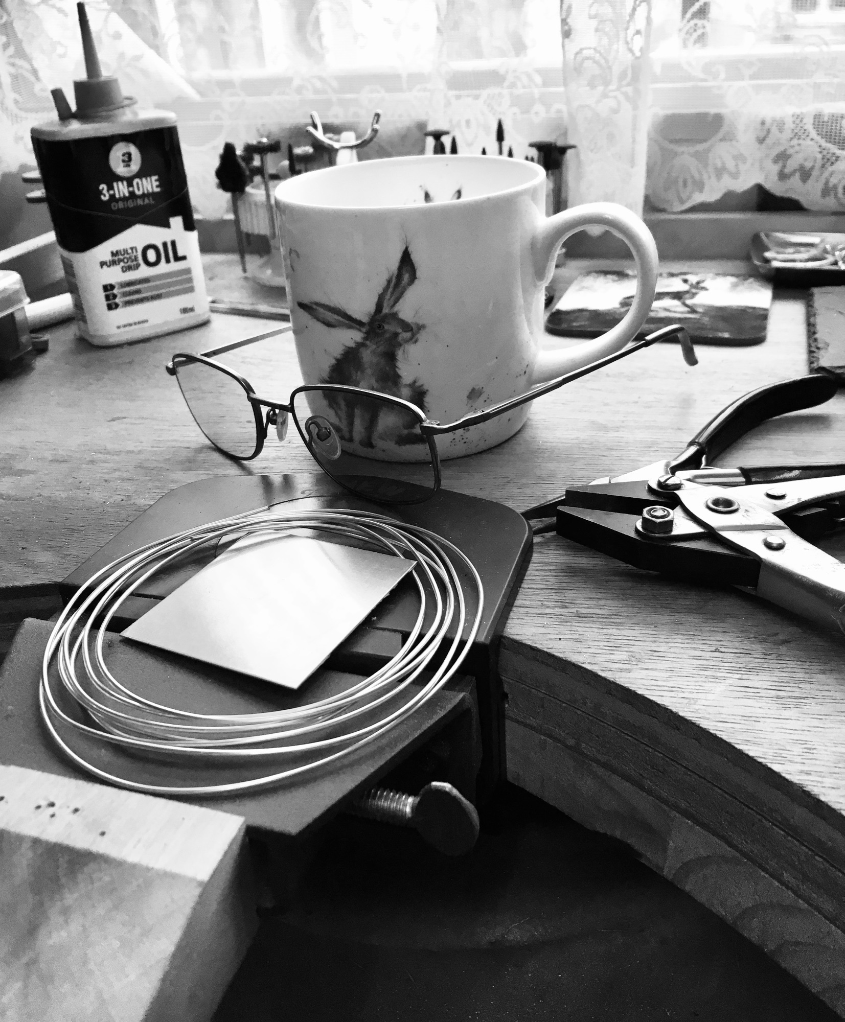 A mug, glasses, tools and sterling silver on a jewellers bench